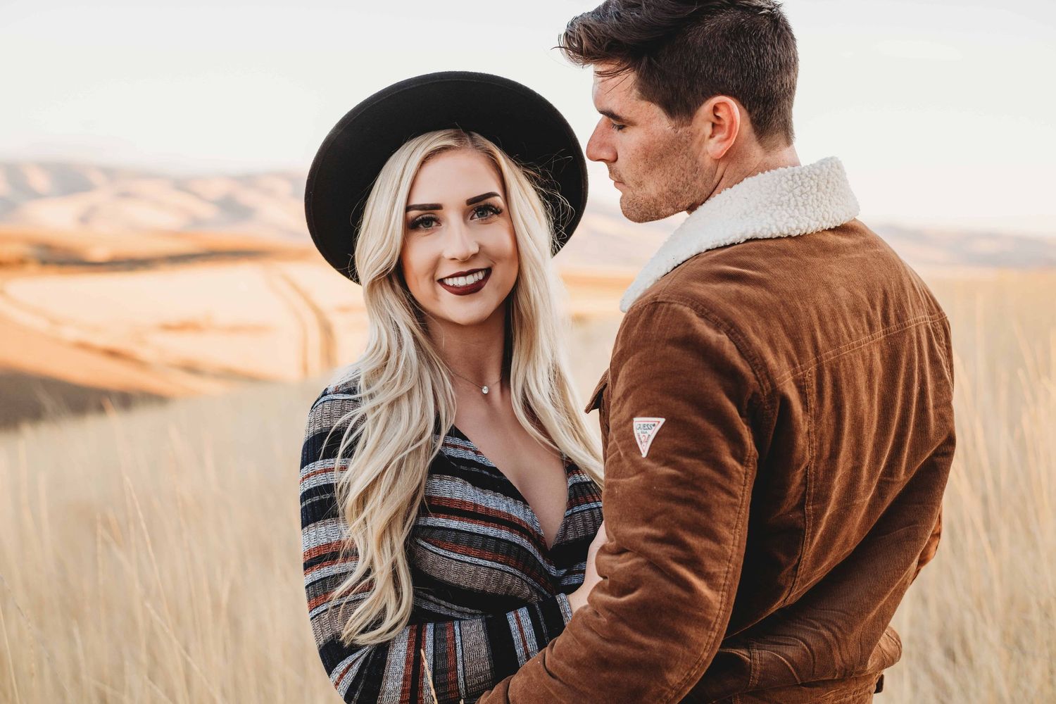 Romantic engagement portrait of a couple standing close together in an open field at golden hour.