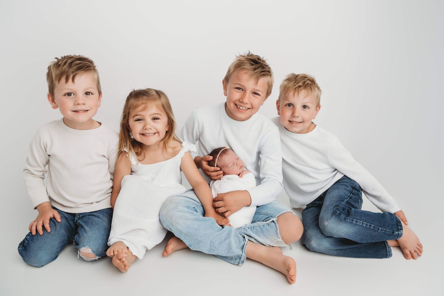 Sibling newborn portrait by a Walla Walla photographer featuring four children sitting together and holding their newborn sibling.