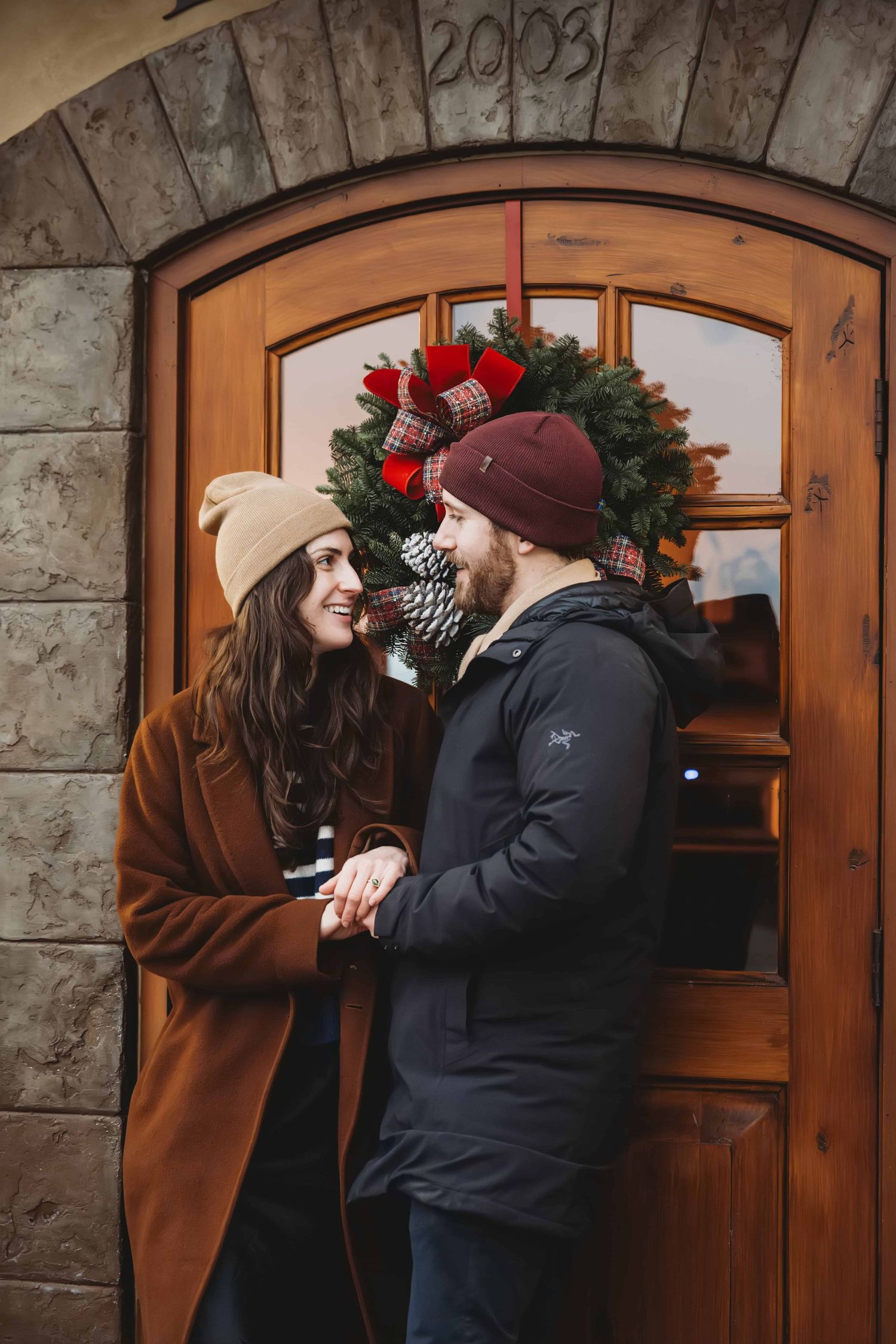 A man and woman standing in front of a winery door with a wintery wreath hanging on the door.