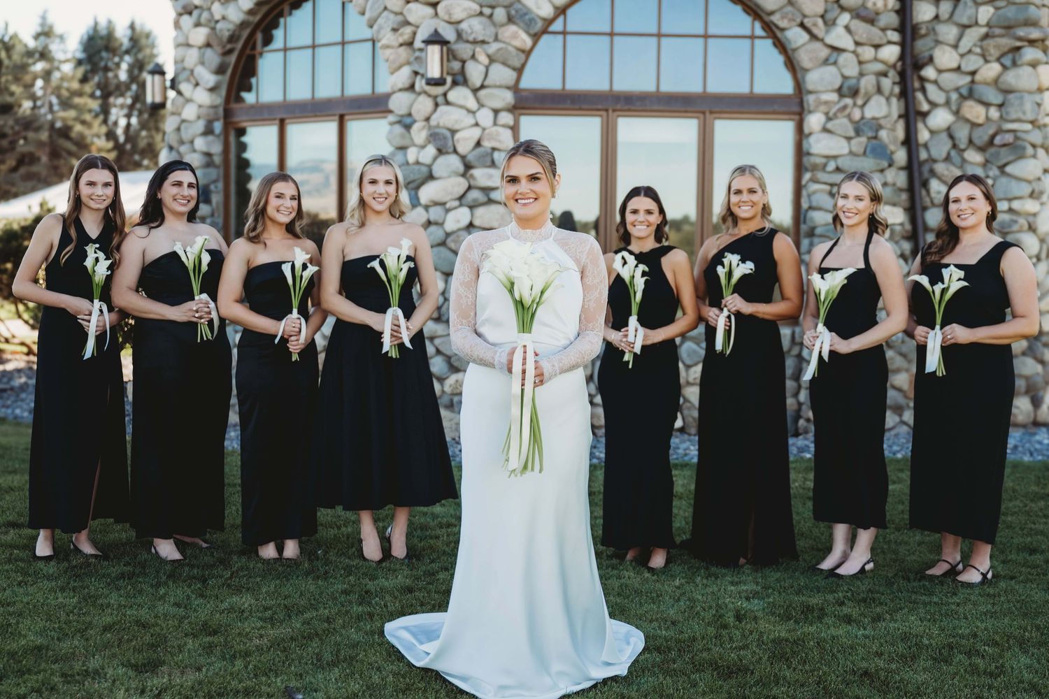 A bride standing in front of her bridesmaids with a stone building in the background.