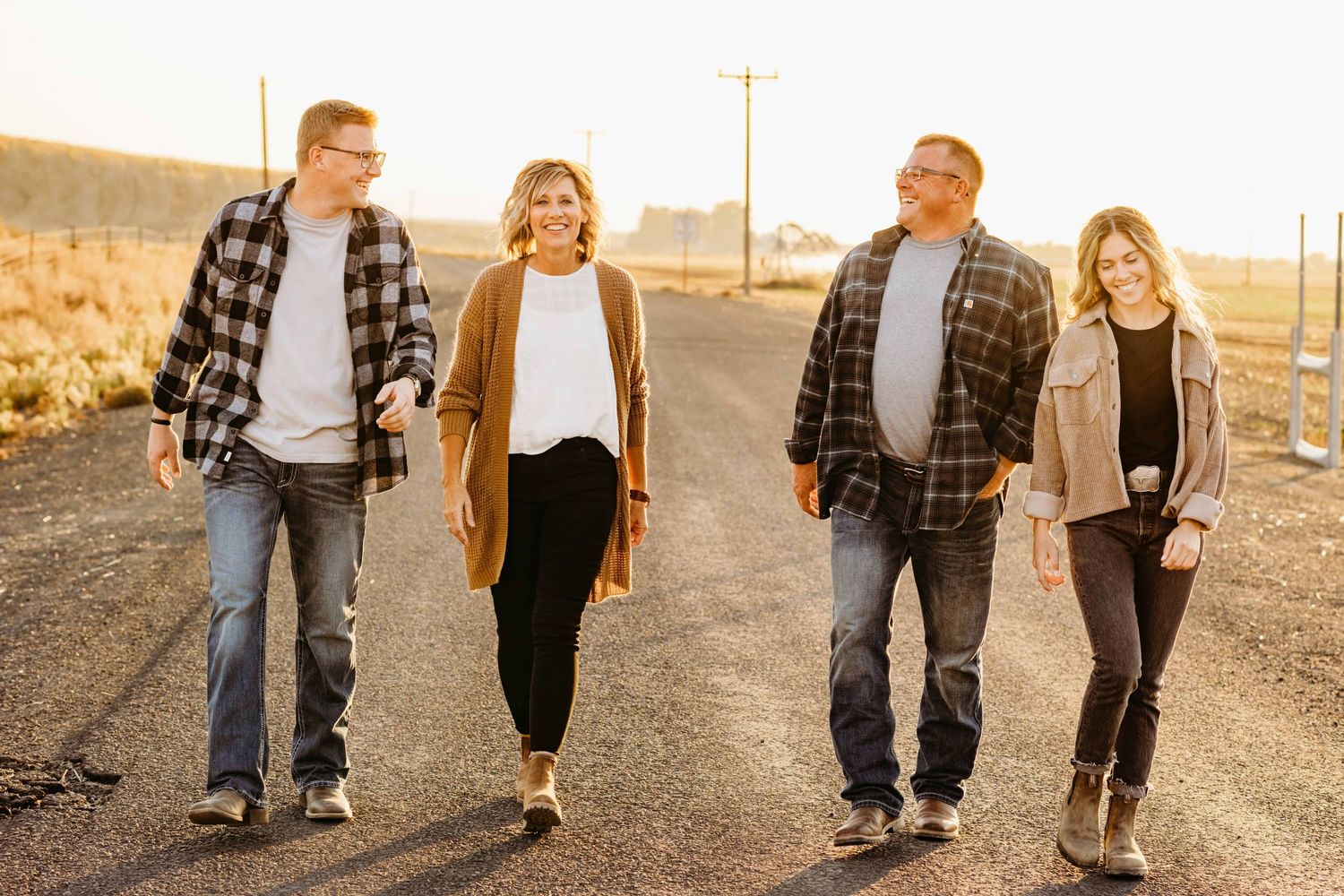 A family portrait of two adult children walking on a road with a golden sunset.