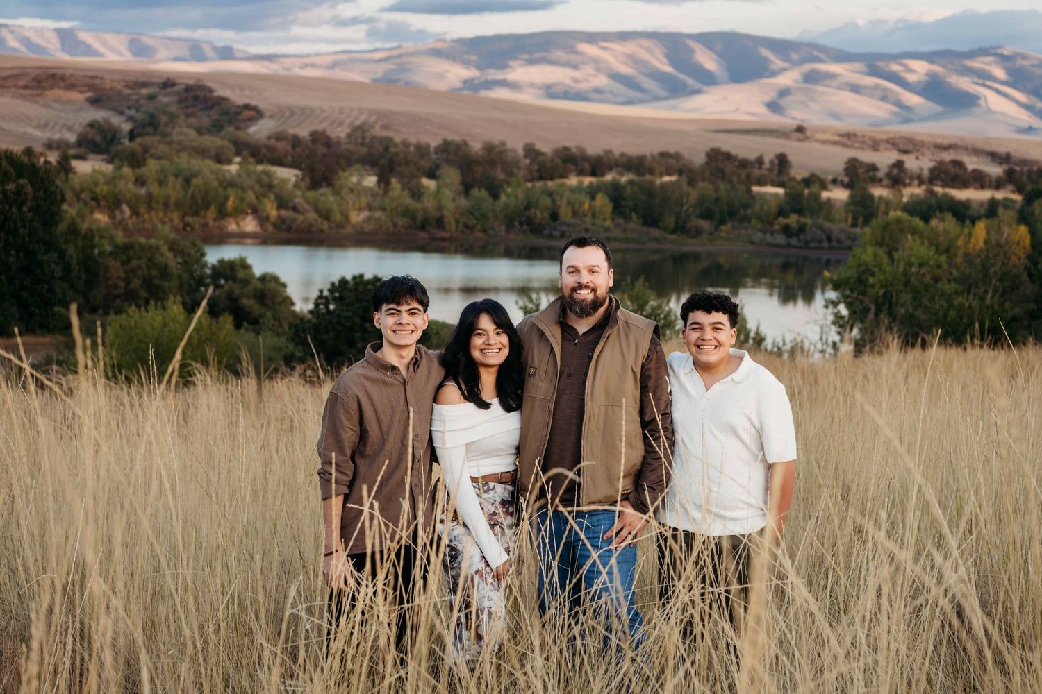 A family dressed in fall colors stands in front of Bennington Lake and smiles for a portrait.