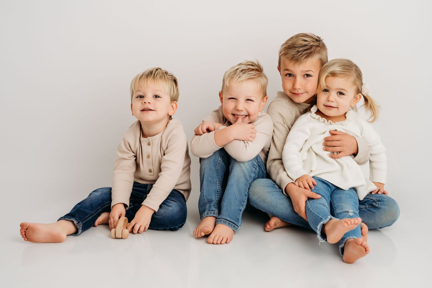 Four children wearing neutral tones sit on a white backdrop in studio.
