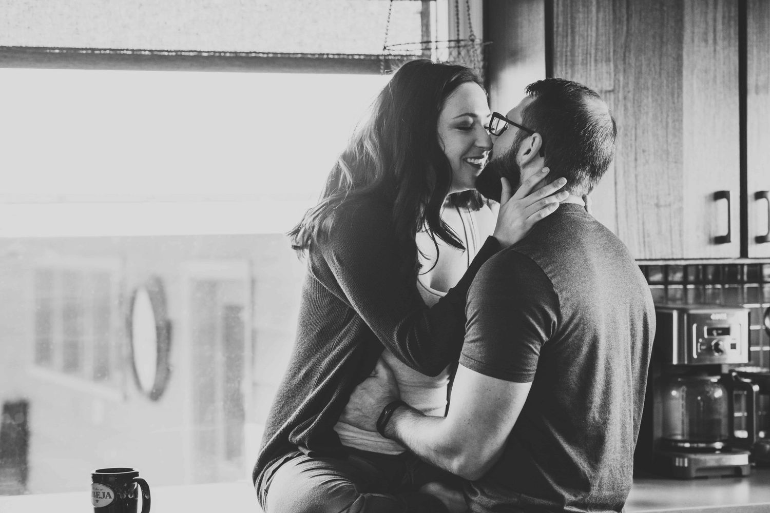 Lifestyle maternity photography in Walla Walla capturing an expectant couple embracing in their kitchen in a candid black and white moment.