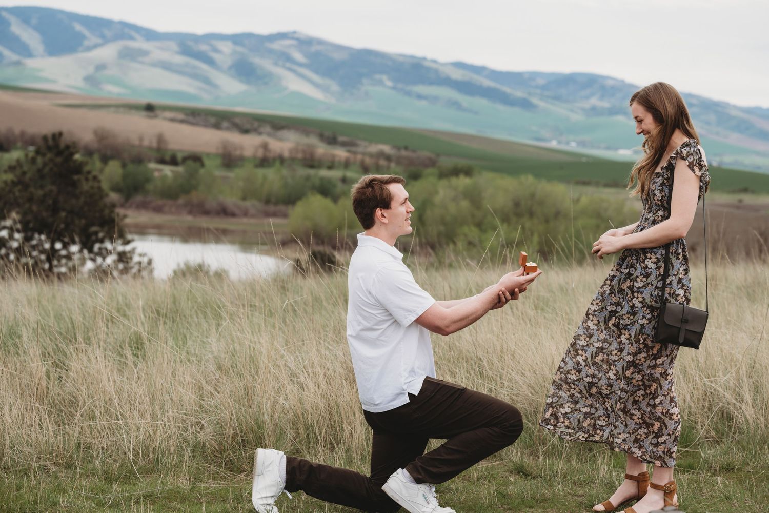 A man on one knee asking his girlfriend to marry him with Bennington Lake and the Blue Mountains in the background in Walla Walla.
