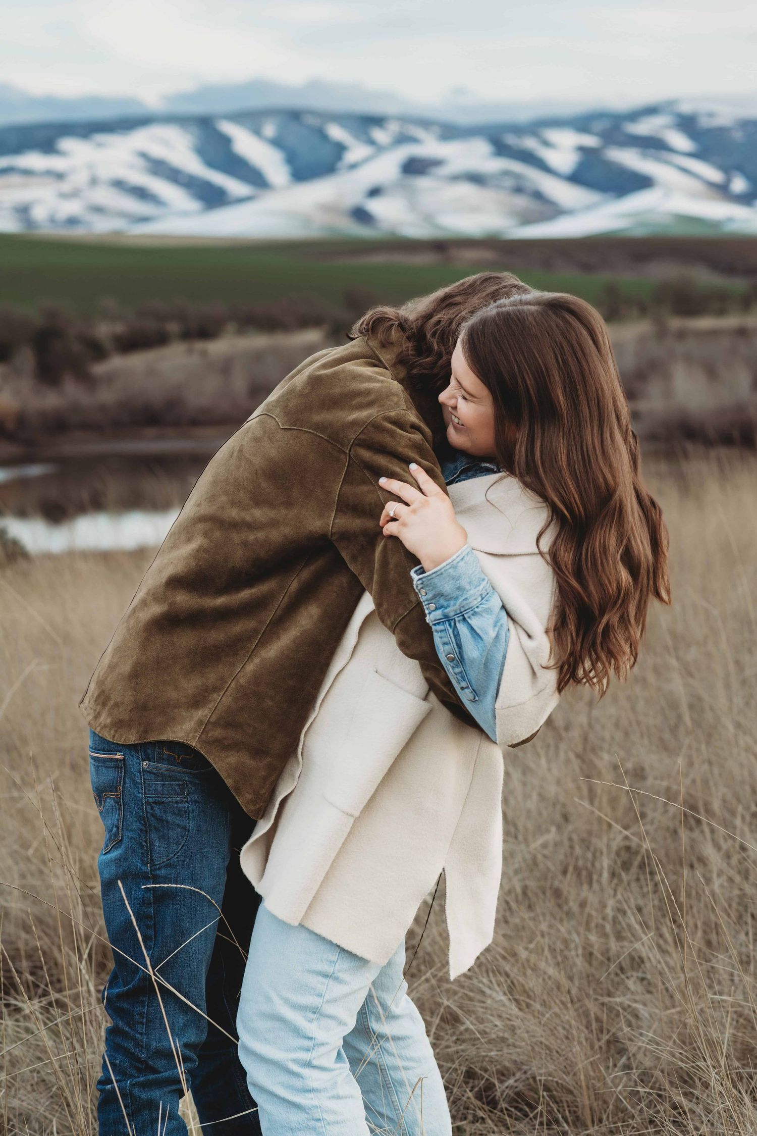 A playful candid picture of a couple with snow capped mountains.