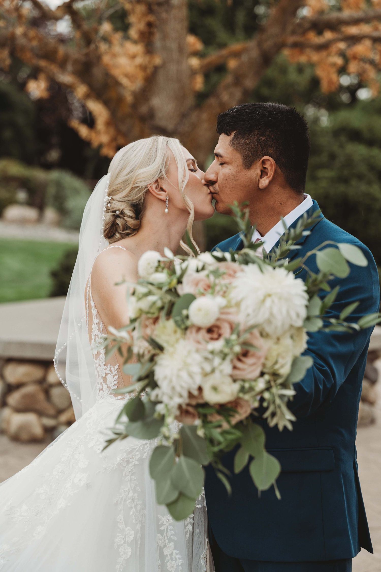 A Walla Walla wedding photographer captured a bride and groom kissing and holding out their bouquet towards the camera.