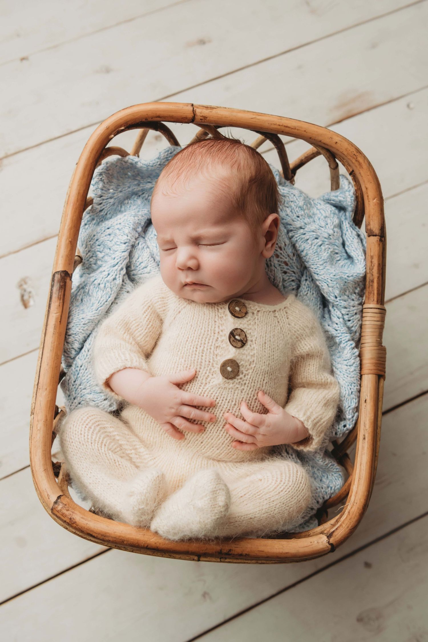 A newborn baby sleeping on a blue blanket in a wicker bassinet.