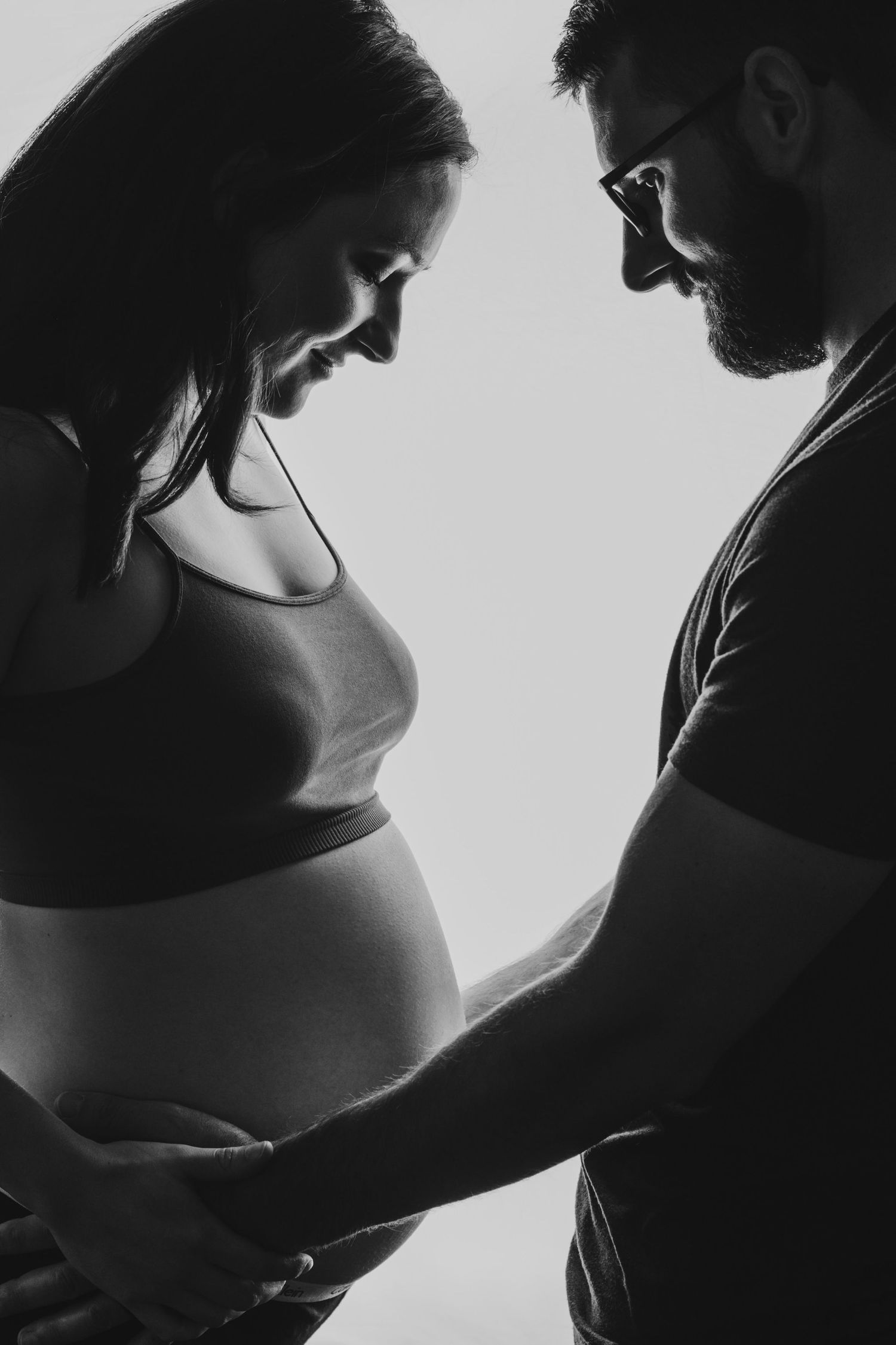 A backlit black and white portrait of a couple expecting their first baby.