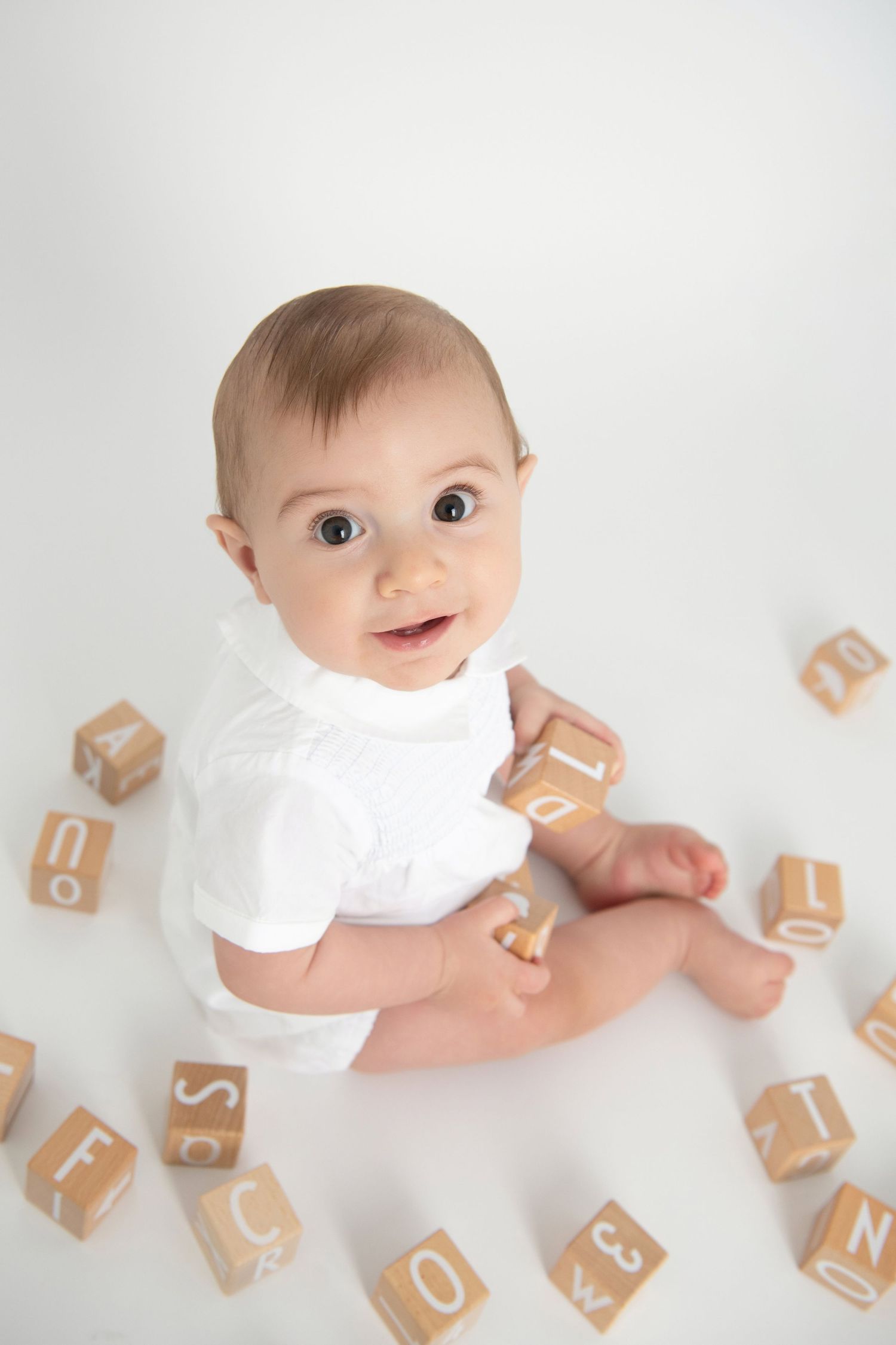 A portrait of a baby boy dressed in white playing with wooden blocks.