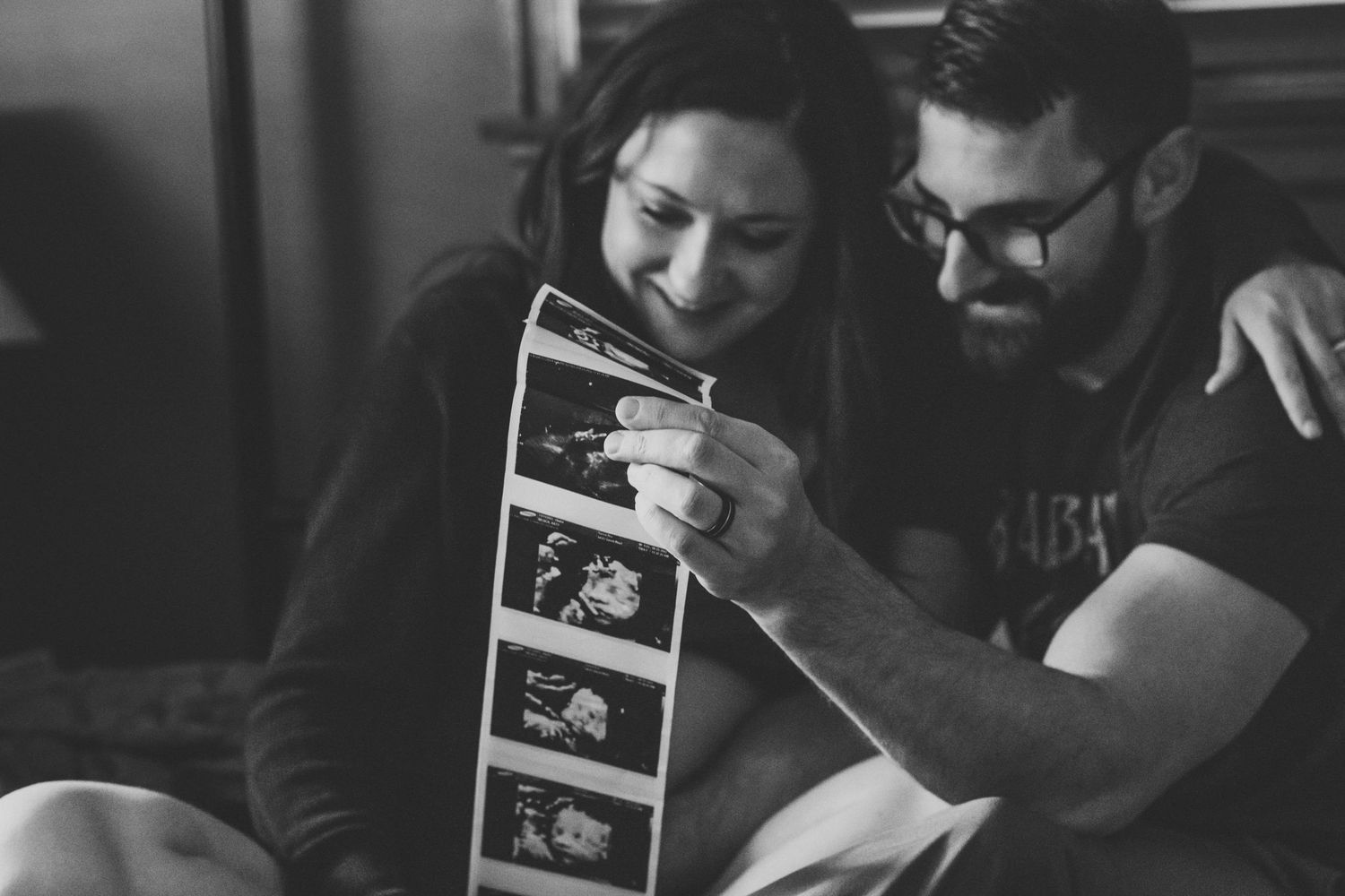 Walla Walla maternity photography session of expectant parents smiling while holding ultrasound photos at home.