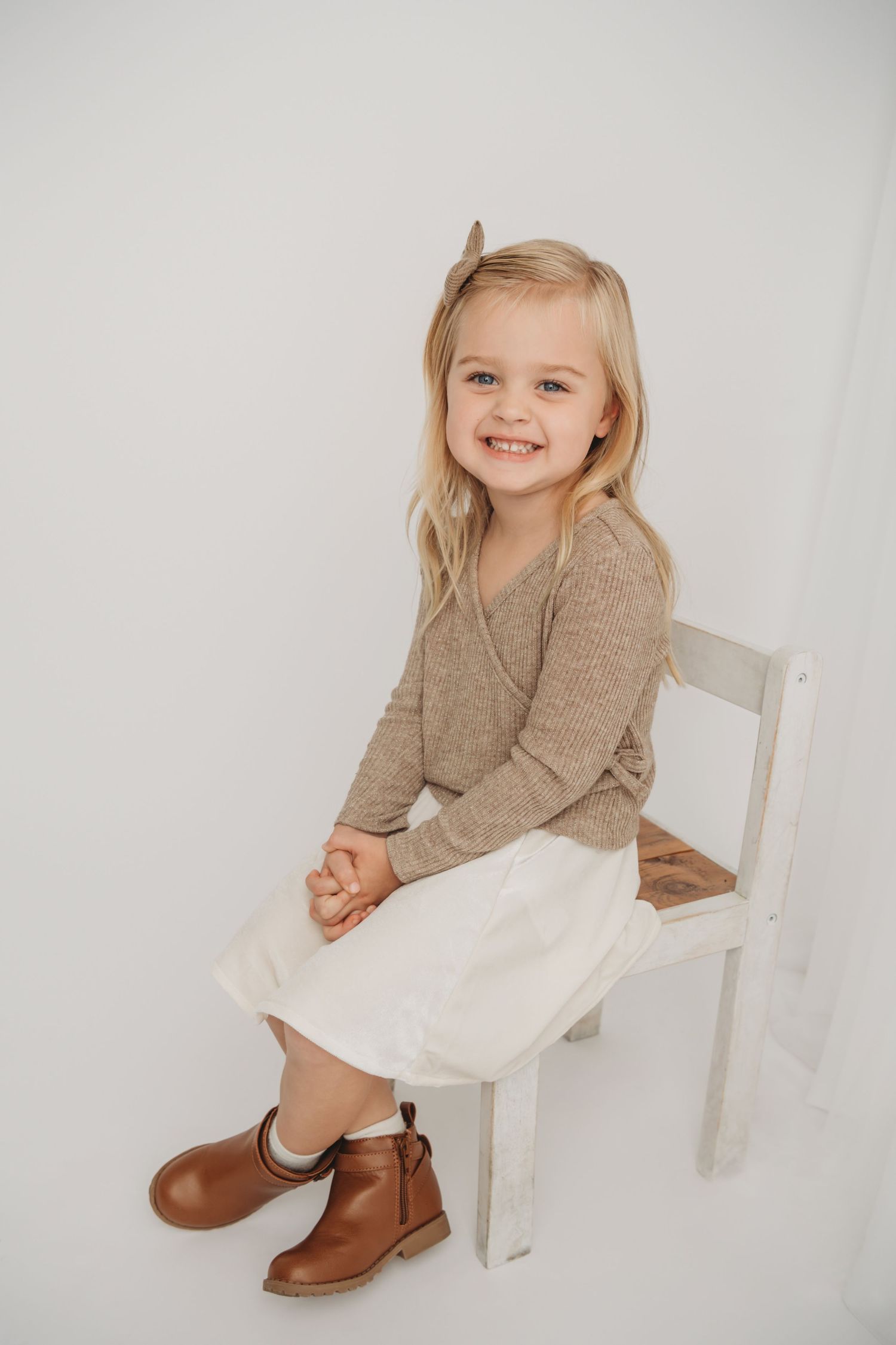 A classic studio portrait of a child sitting on a white wooden chair.