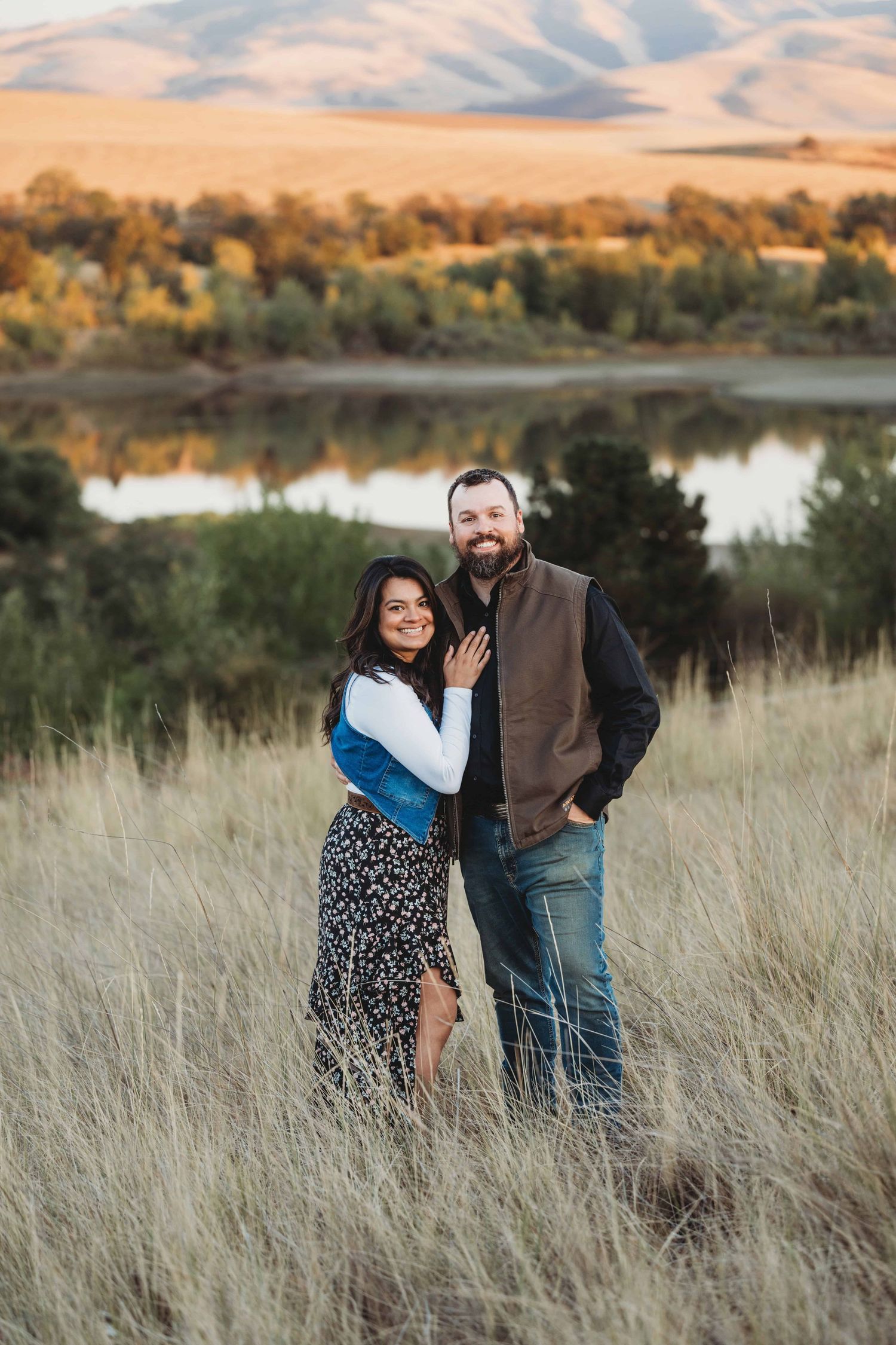 A couple standing in front of a lake with fall colors.