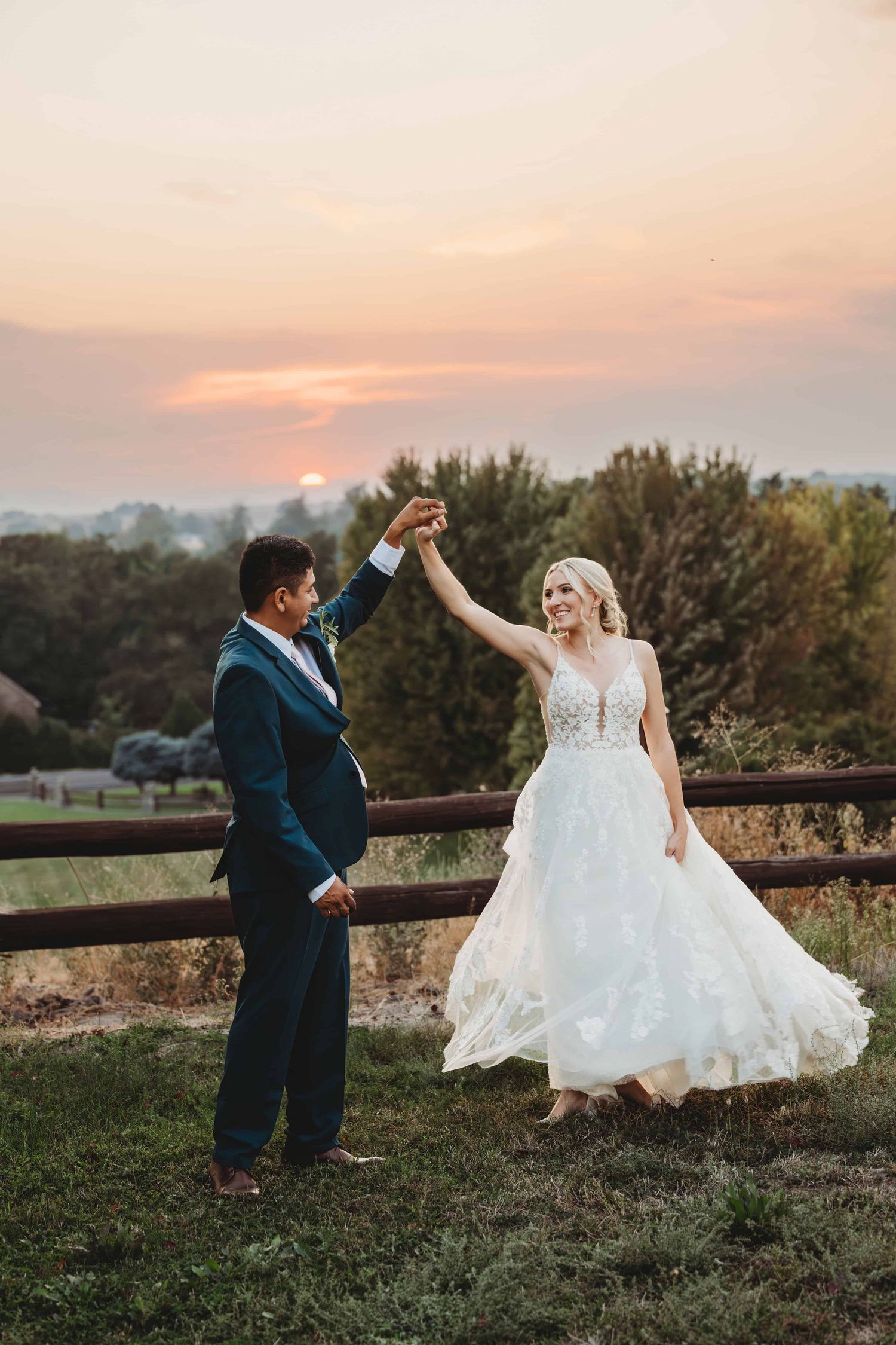A bride and groom dancing during sunset near a wooden fence.