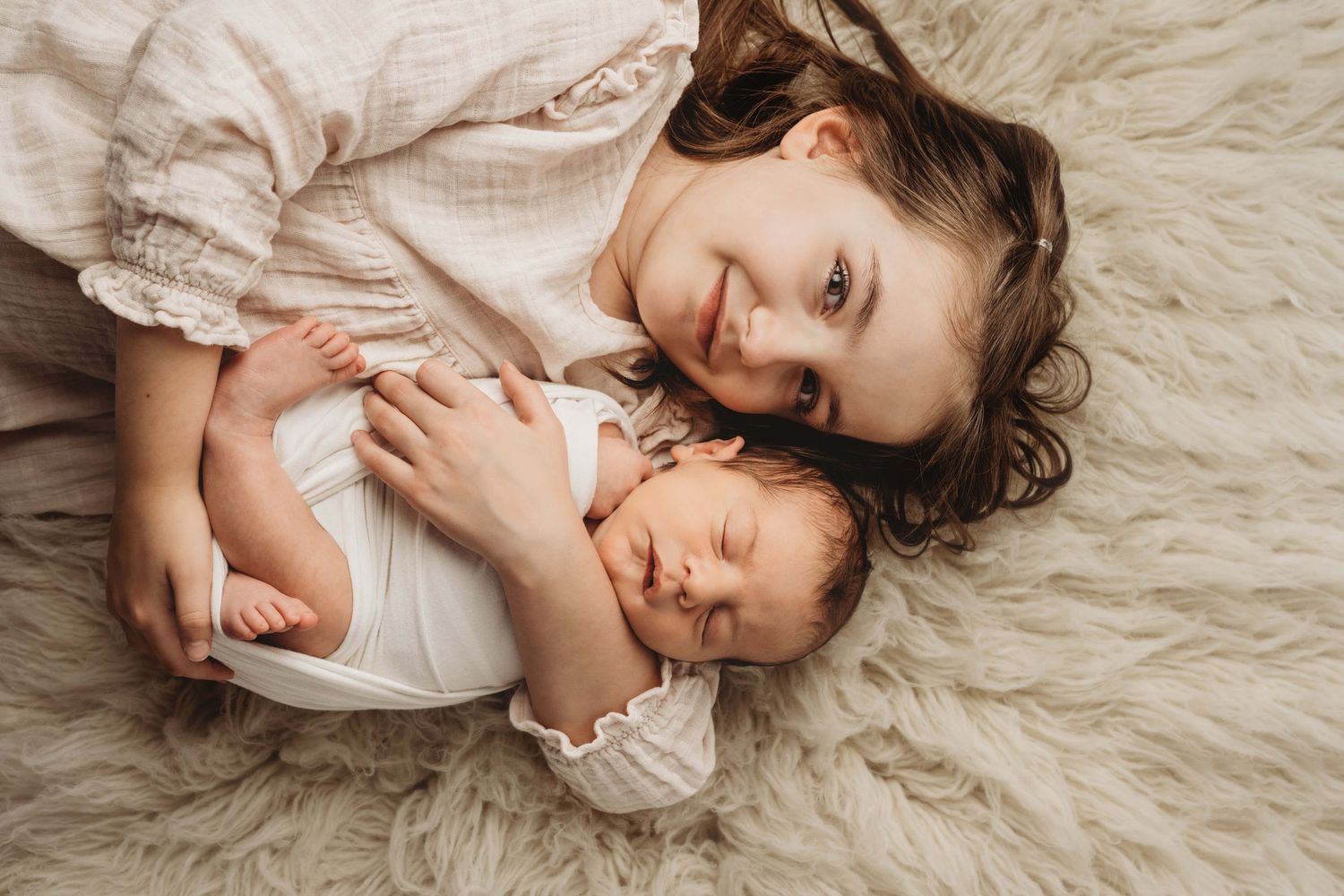 A big sister holding her newborn baby brother as he sleeps.