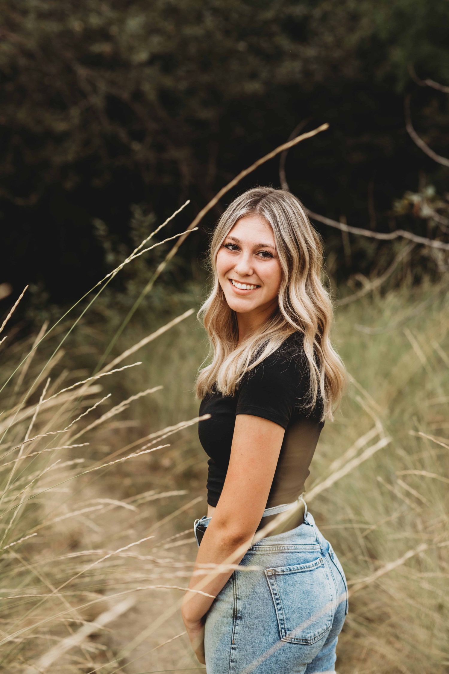 A portrait of a senior standing among tall grasses wearing a black shirt and jeans, taken by a Walla Walla photographer.