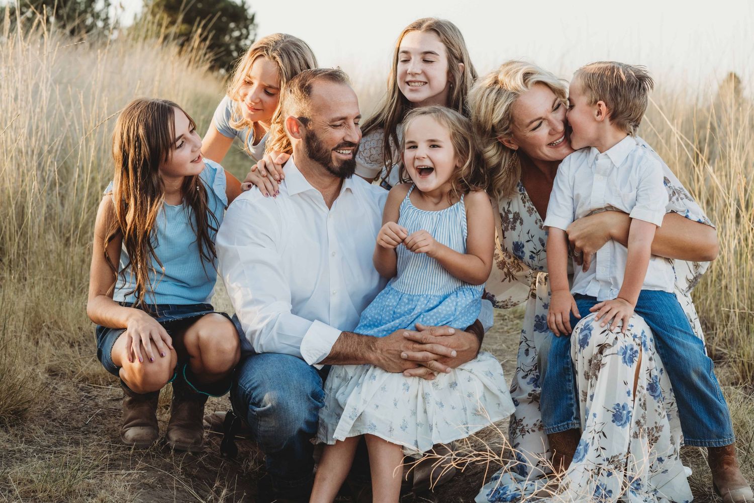 Candid family portrait by a Walla Walla photographer featuring parents and children laughing together in tall grass.