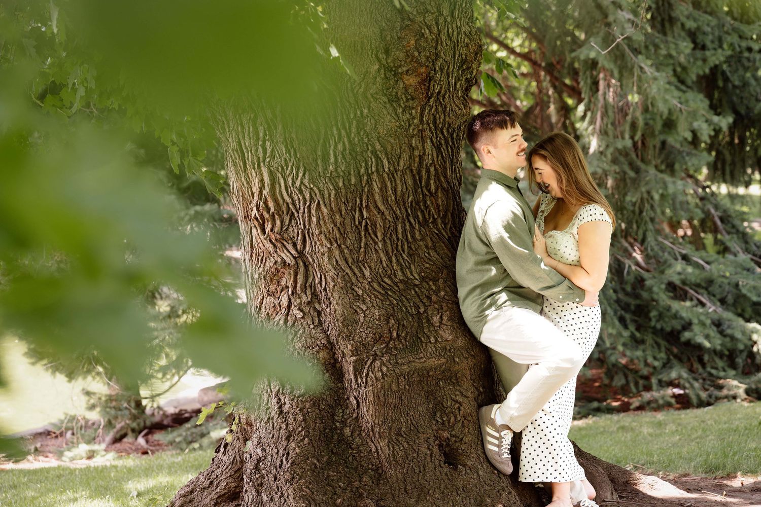 A man leaning against a tree as his girlfriend hugs him.