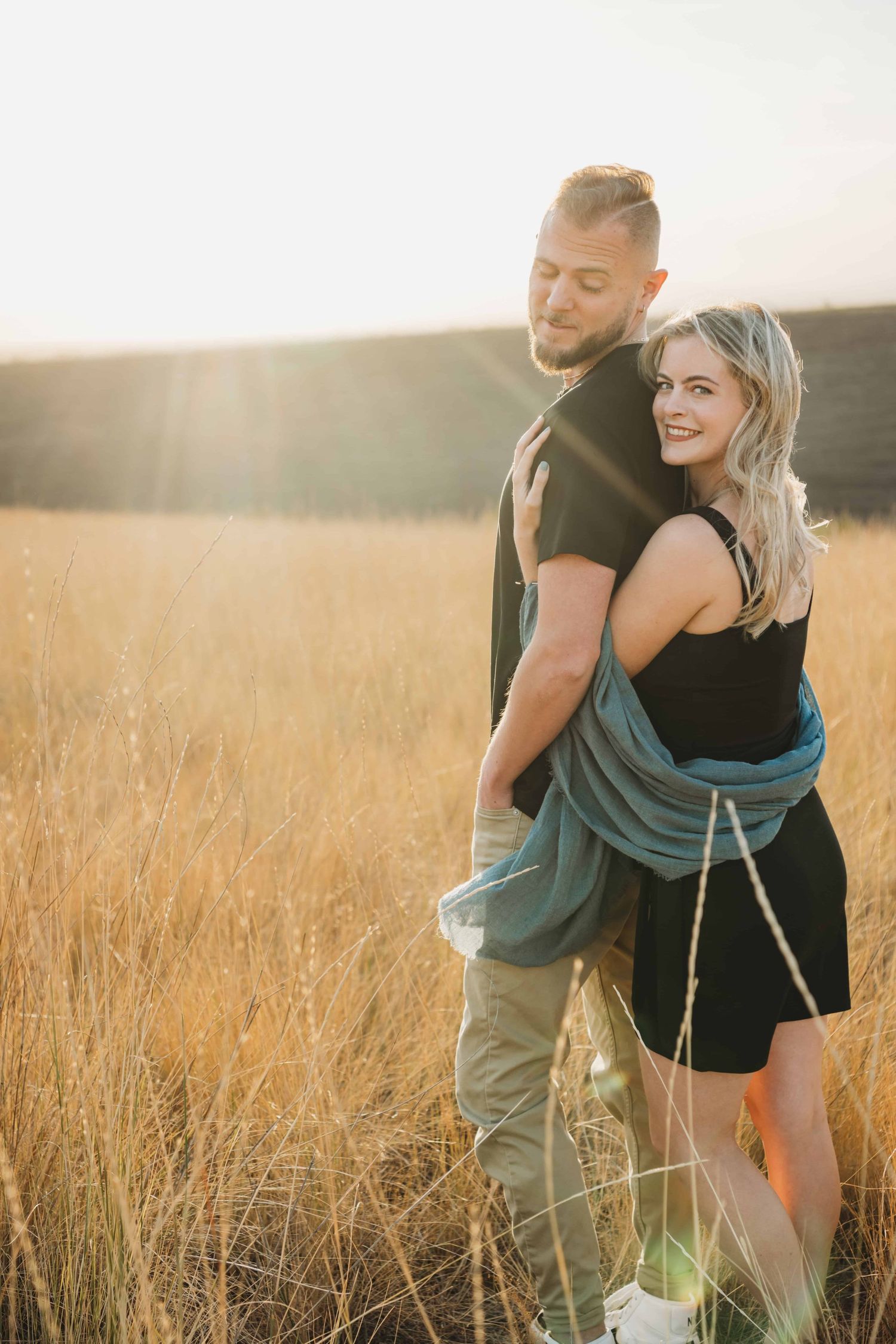 A woman hugging her husband as he looks back at her and smiles in a golden hour portrait.