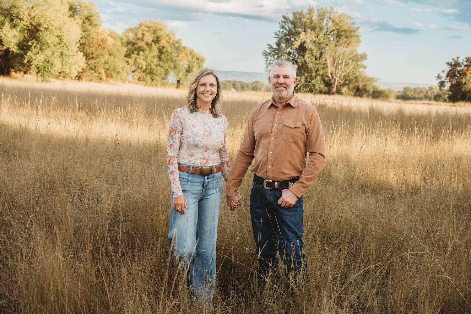 A couple walking through a tall grassy field.