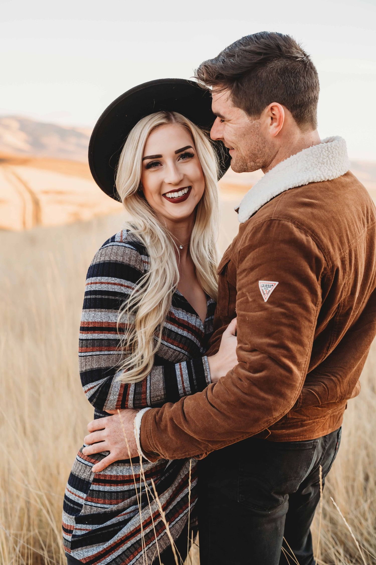 A man looking at his girlfriend who's wearing a hat, smiling at the camera.