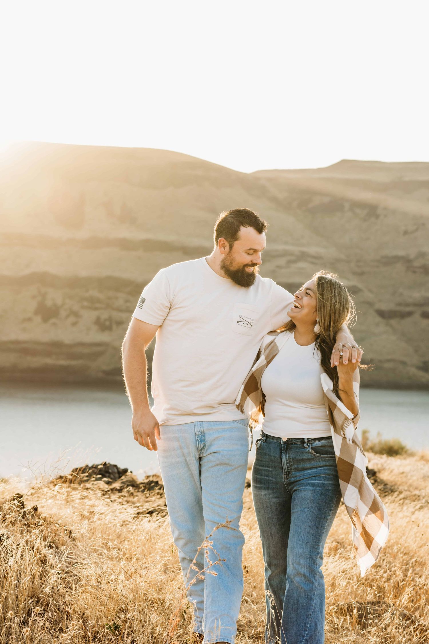 A couple walking with the man's arm around the woman's shoulder and laughing together.