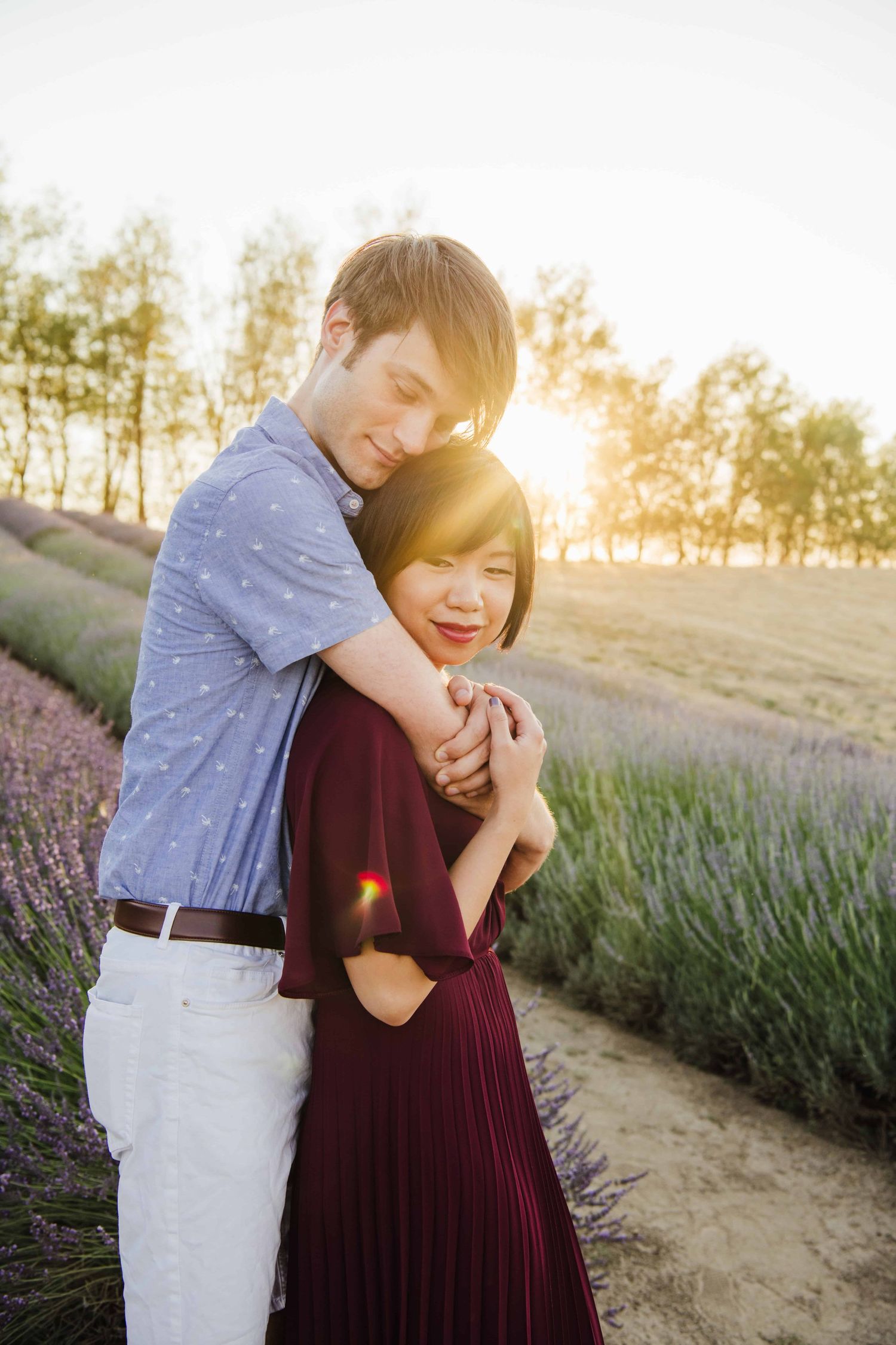 Engaged couple hugging and smiling in a lavender field at sunset.