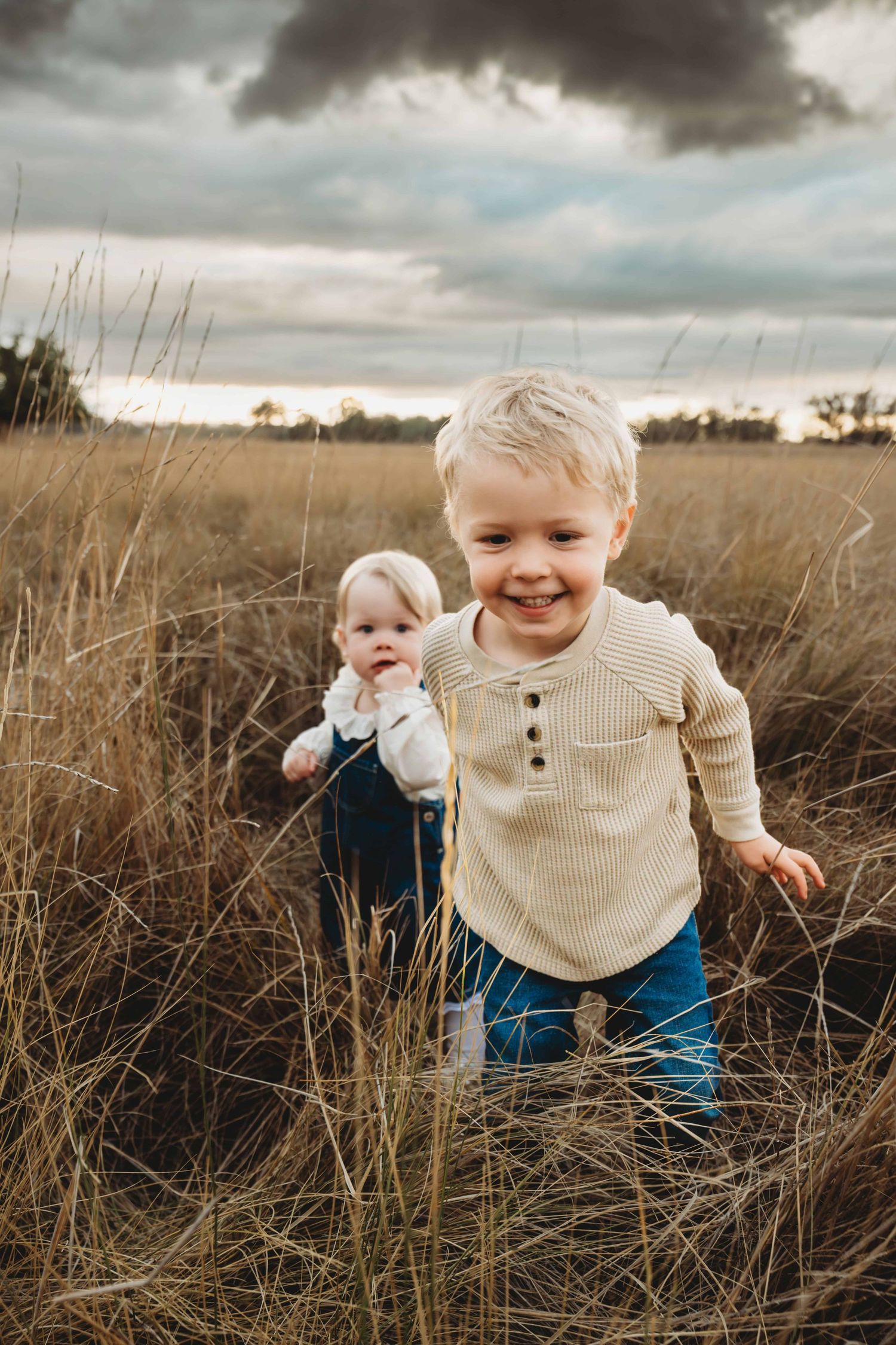 A moody portrait of two children running through a field with a stormy sunset taken by a Walla Walla photographer.