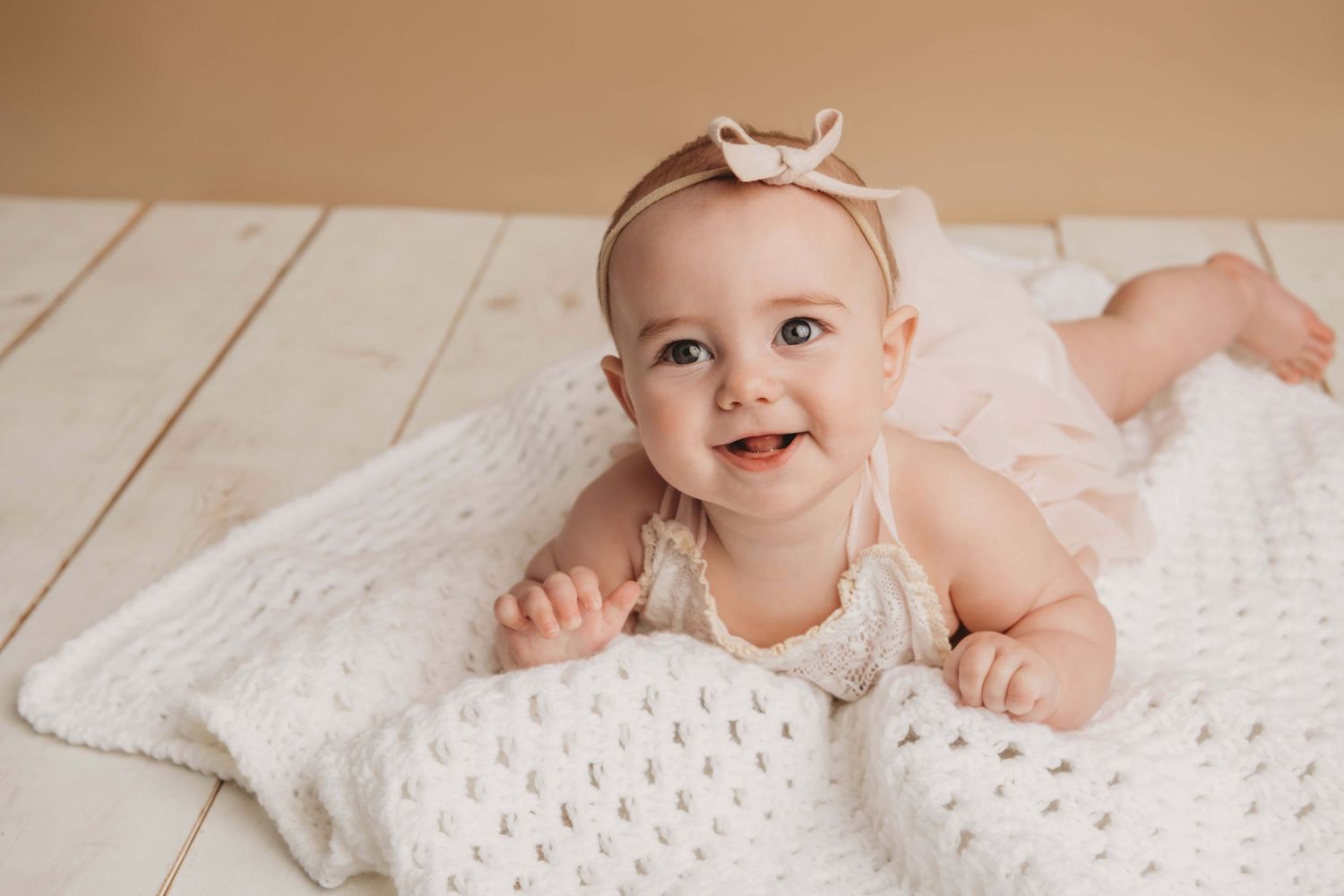 A baby laying on her stomach on a handmade white blanket.