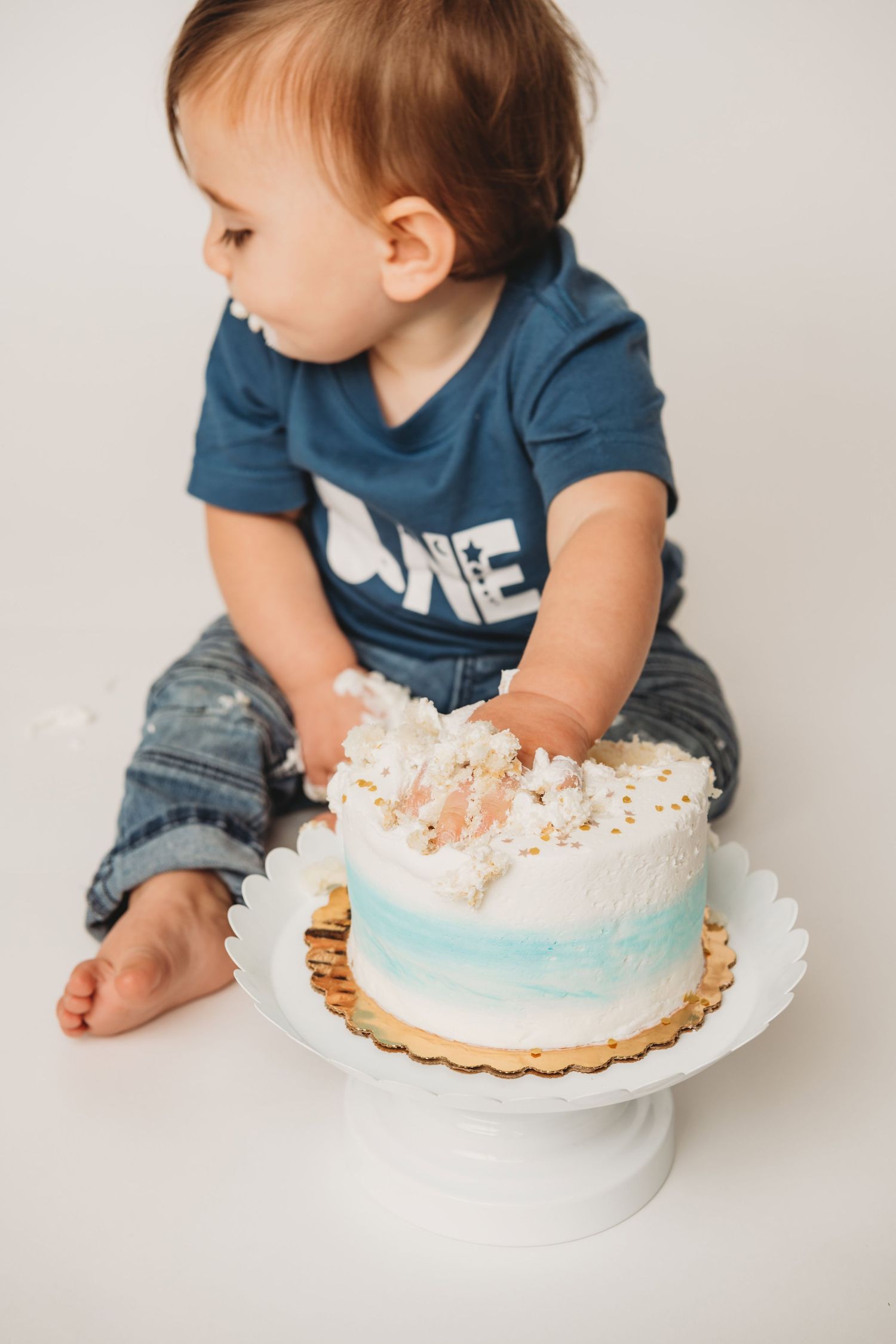 A one year old smashing a white and blue cake.