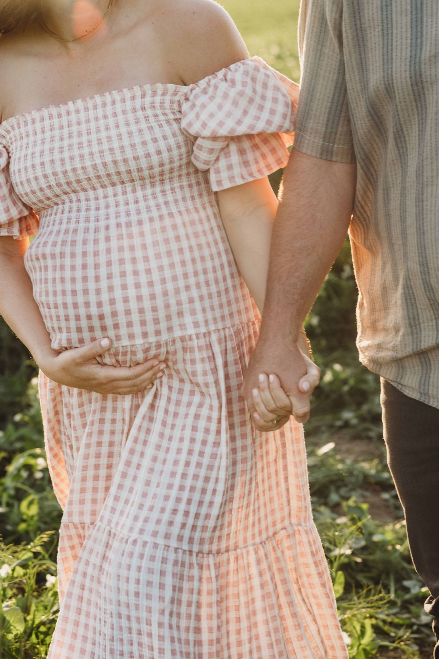 A close up photo of a pregnant woman holding hands with her husband while walking in a pea field.