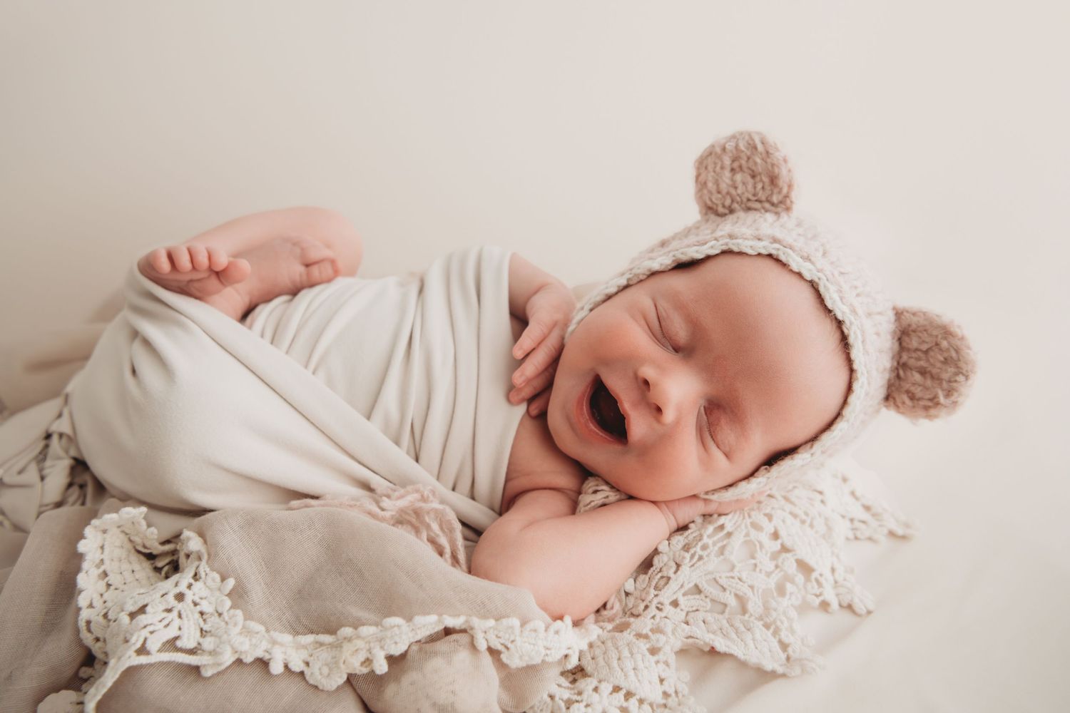 A baby girl sleeping wearing a bear ear bonnet and smiling.