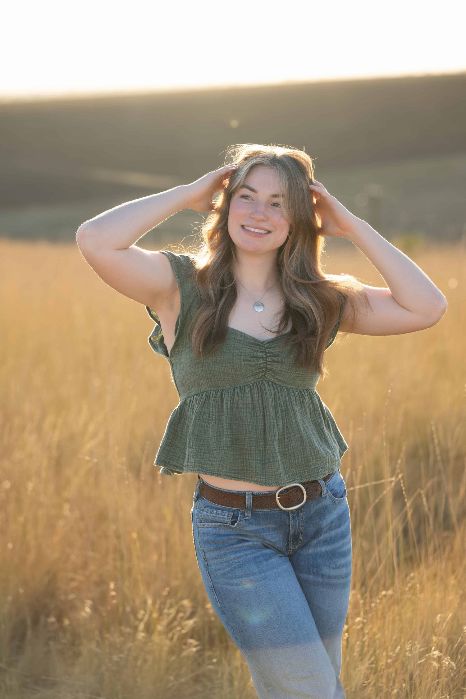 A portrait of a high school senior looking off into the distance while she runs her hands through her hair at Bennington Lake in Walla Walla