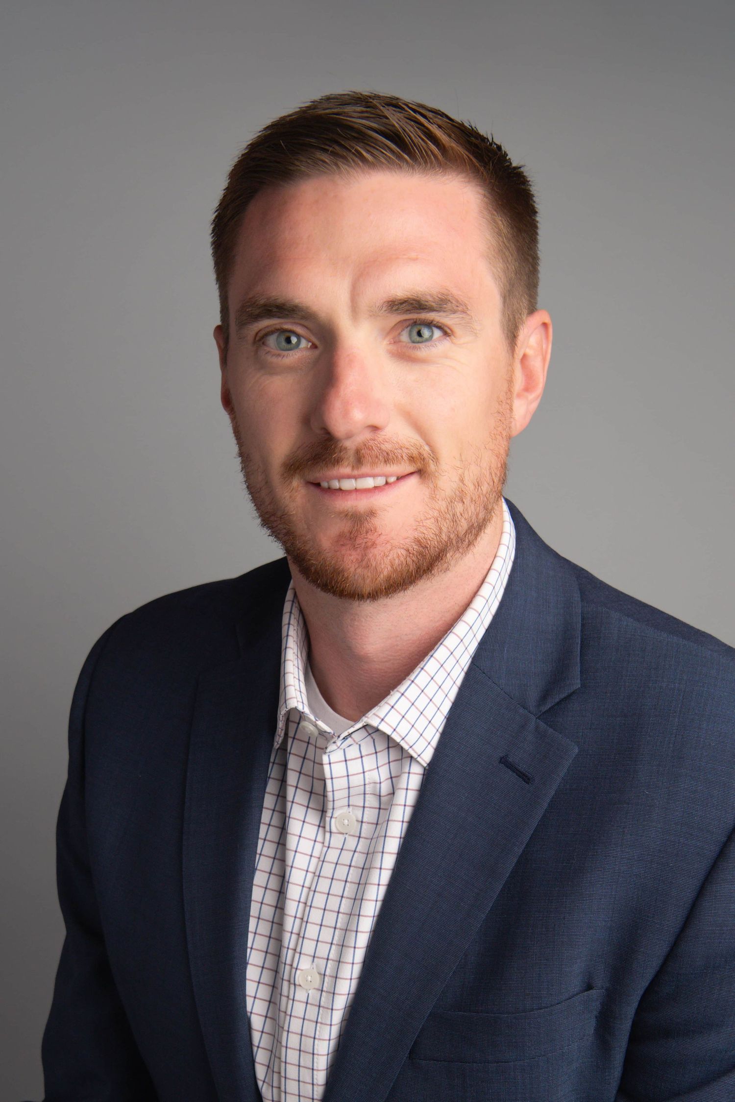A classic headshot of a business professional wearing a suit jacket on a gray background.