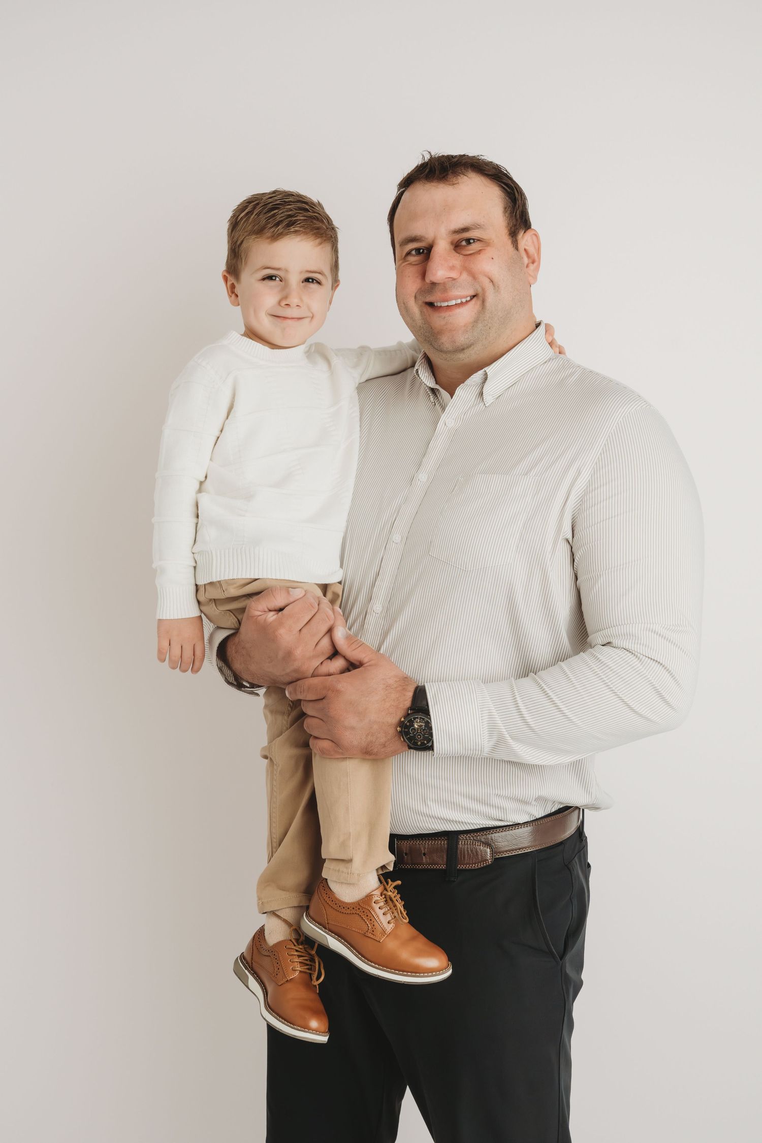 A dad and his son wearing neutral colors look at the camera and smile.