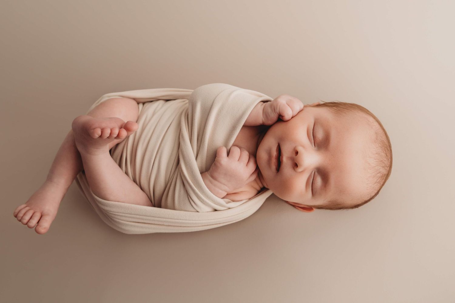 A newborn laying on a neutral backdrop sleeping.