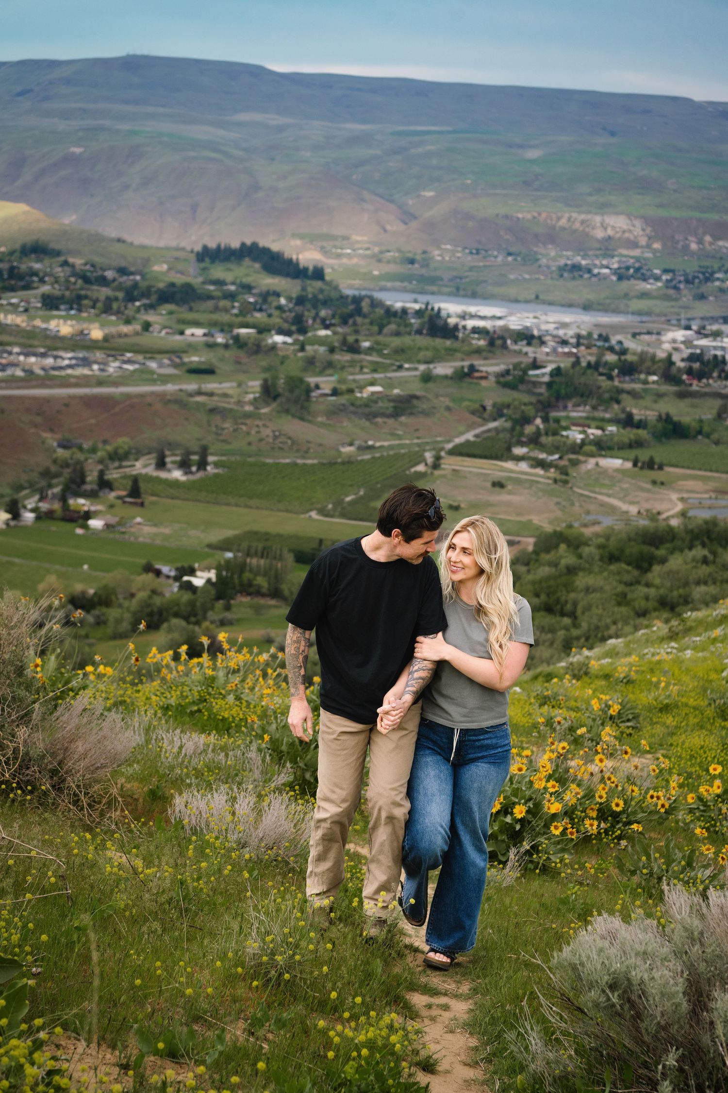 A Wenatchee photographer captures a couple walking on a path through the wildflowers at Sage Hills in Wenatchee Washington.
