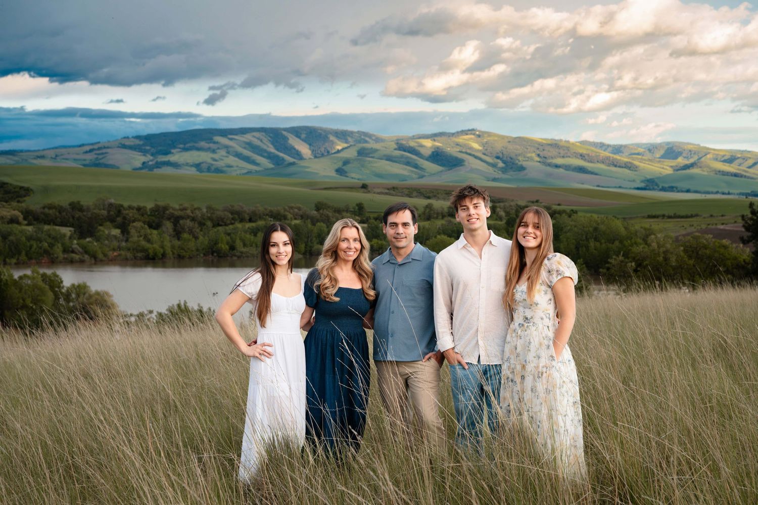 A family portrait with a dramatic sunset and blue mountains behind them, taken by a Wenatchee photographer.