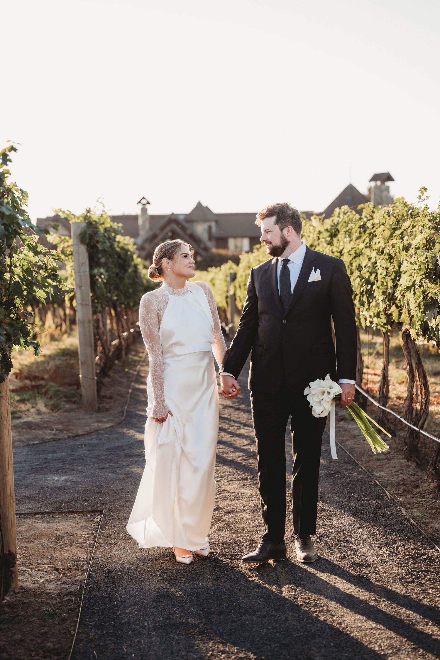 A portrait of a bride and groom walking through a vineyard holding hands at Yellow Hawk Resort taken by a Walla Walla wedding photographer.