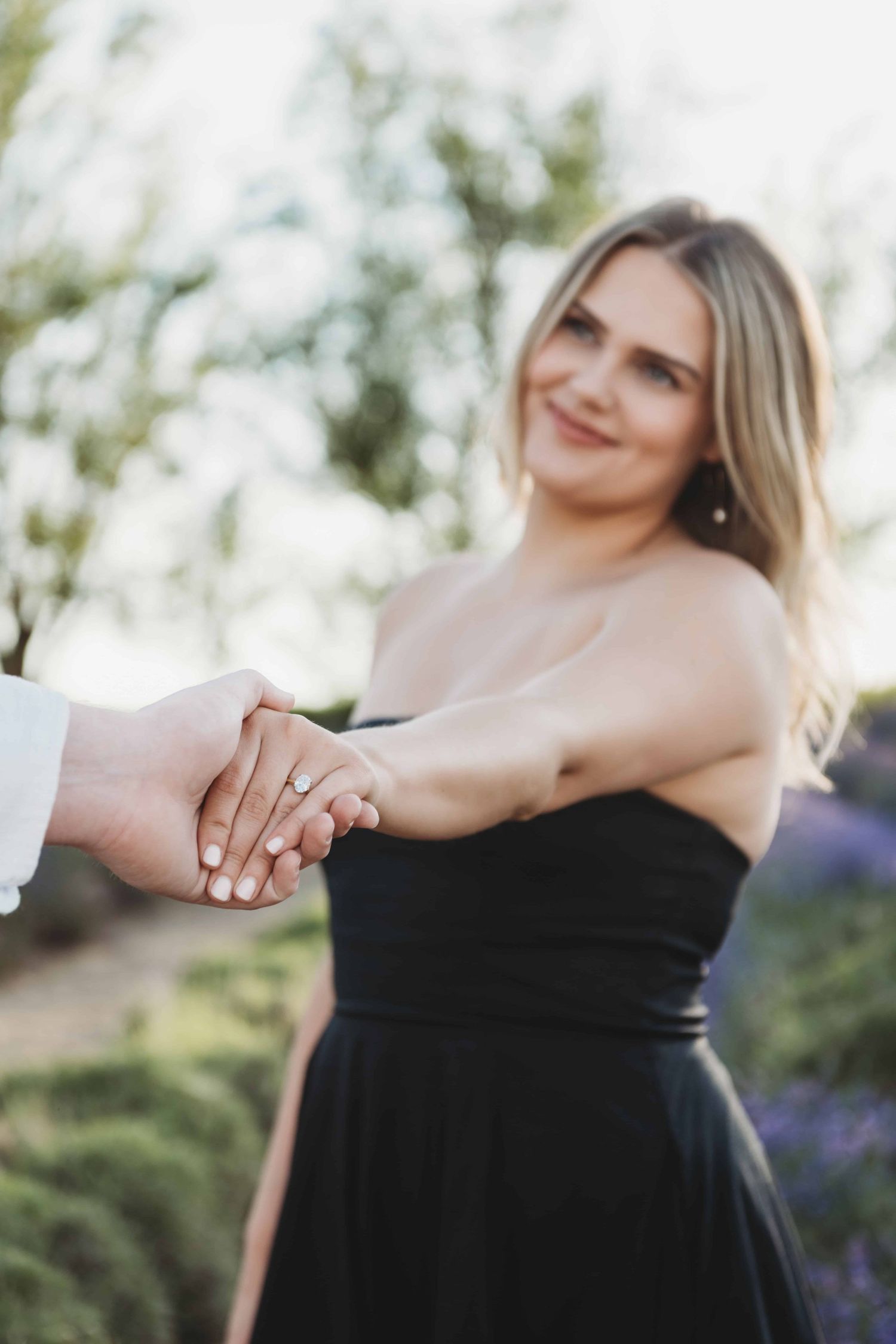 An engaged woman holding her fiance's hand and looking at him with a soft smile on her face.