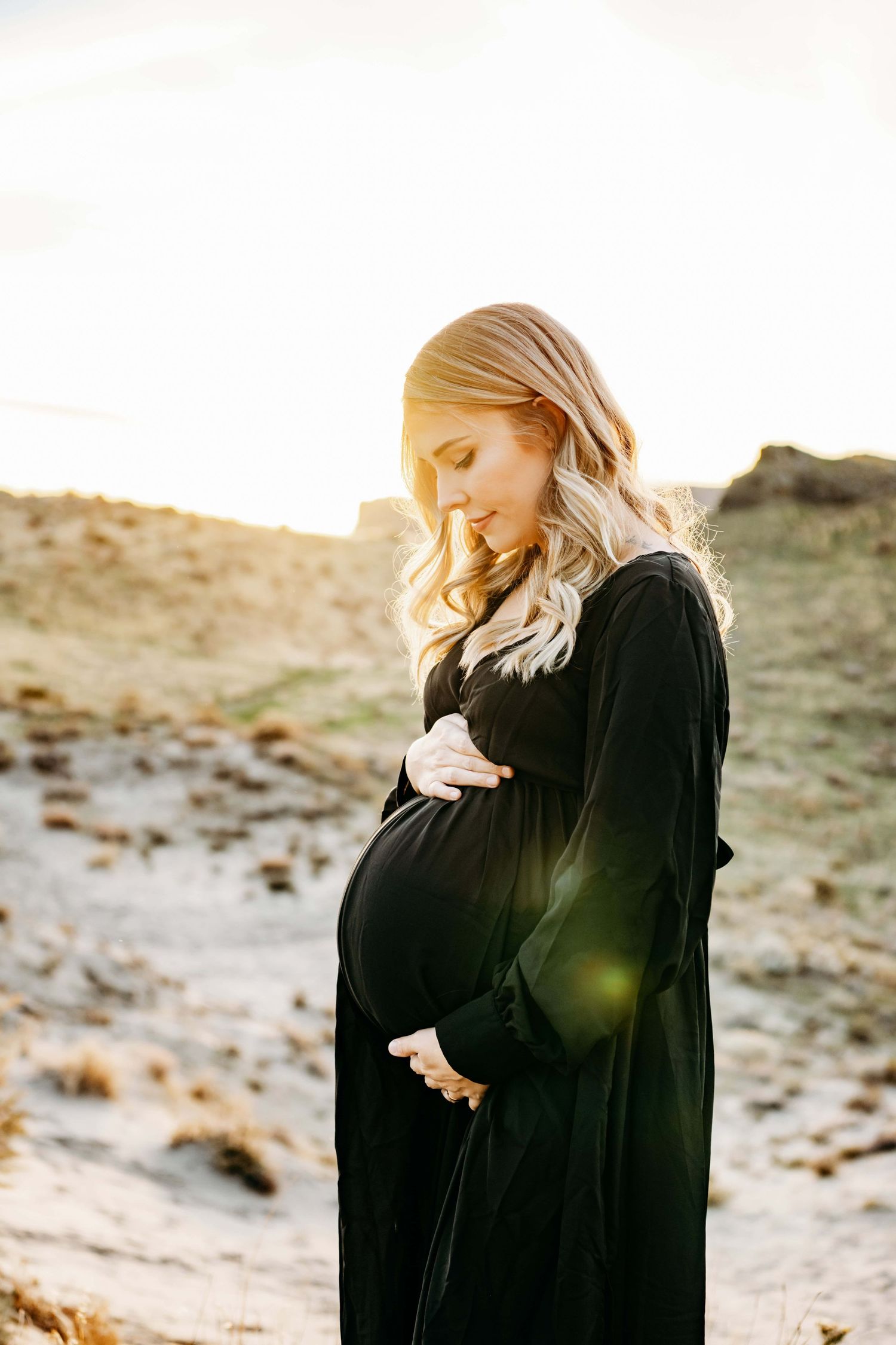 A Walla Walla photographer captures an expectant mother in a black dress, holding her belly and softly smiling.