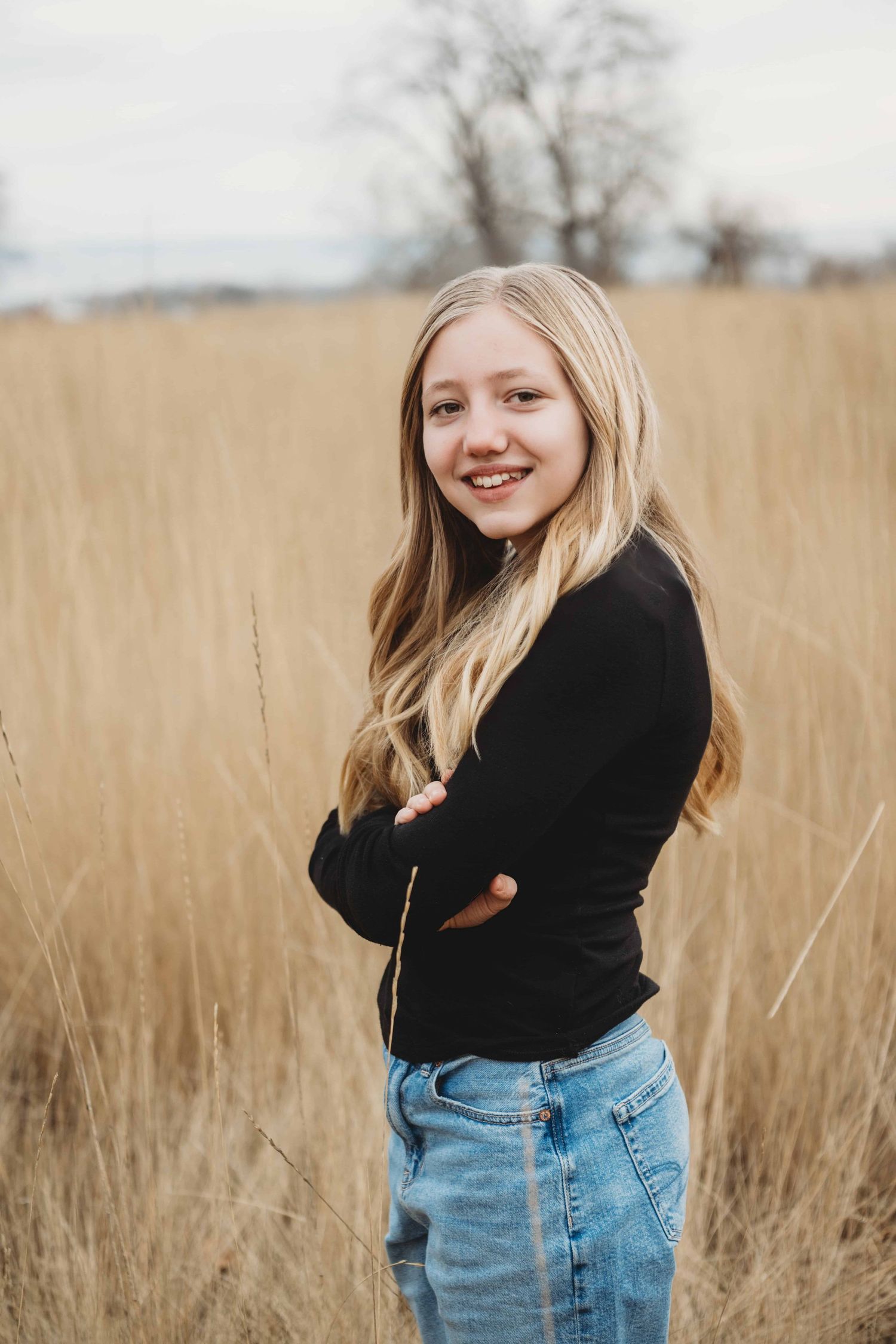 A portrait of a girl standing in a field wearing a black shirt and jeans with a natural smile.