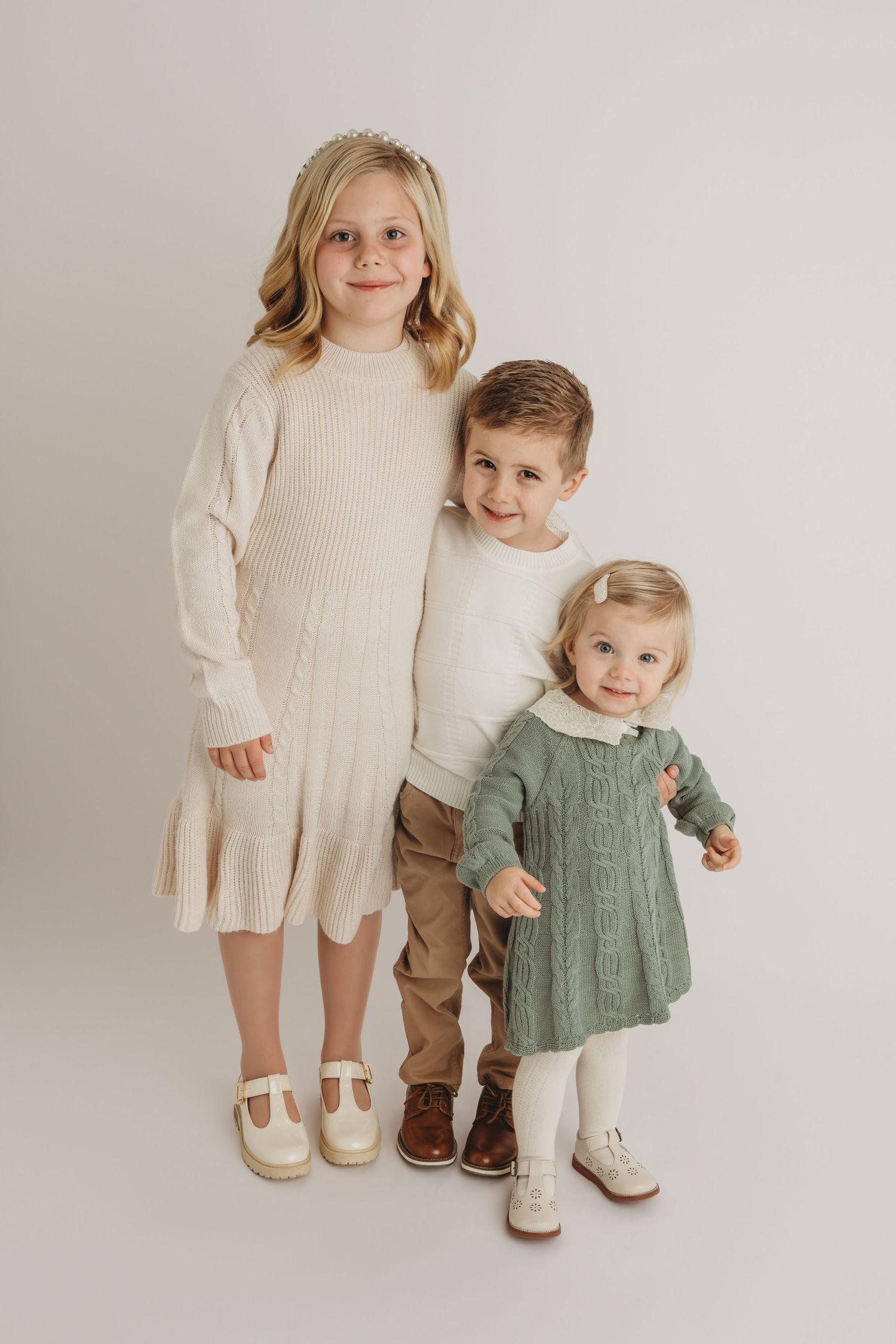 Three children stand together and smile for the camera.