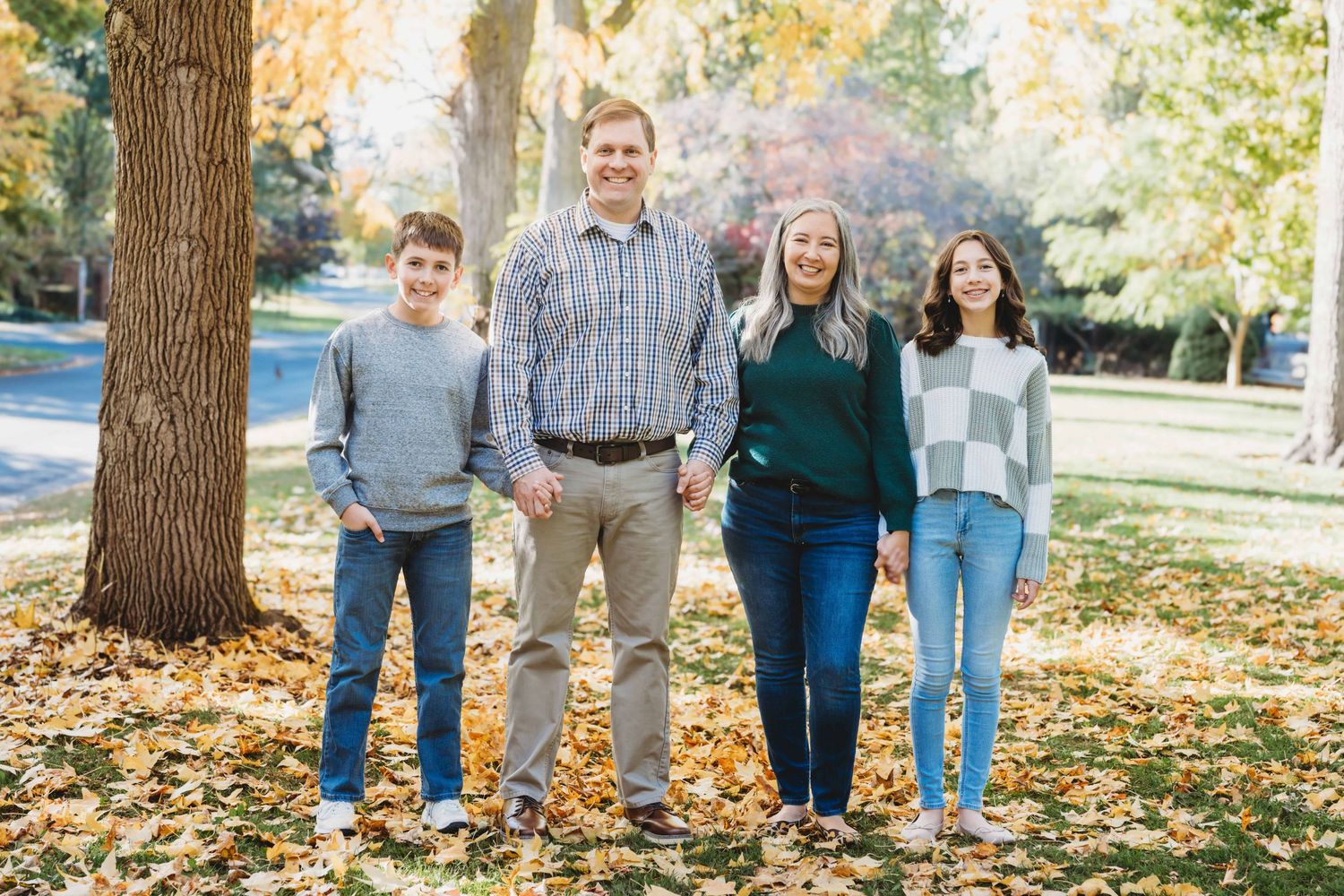A family of four standing together holding hands surrounded by fall leaves at Whitman College in Walla Walla.