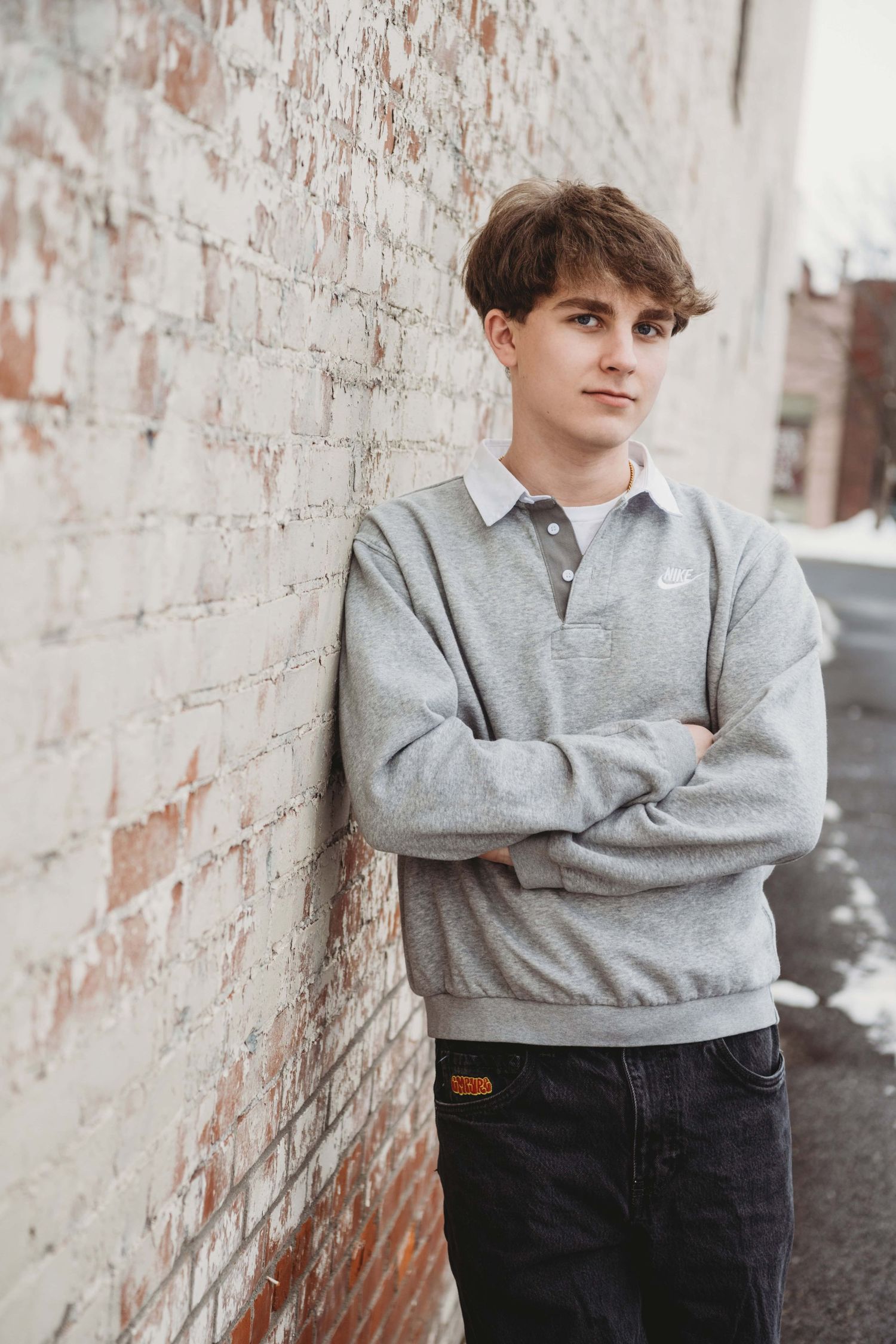 A senior portrait of a guy leaning against a brick wall and looking at the camera.
