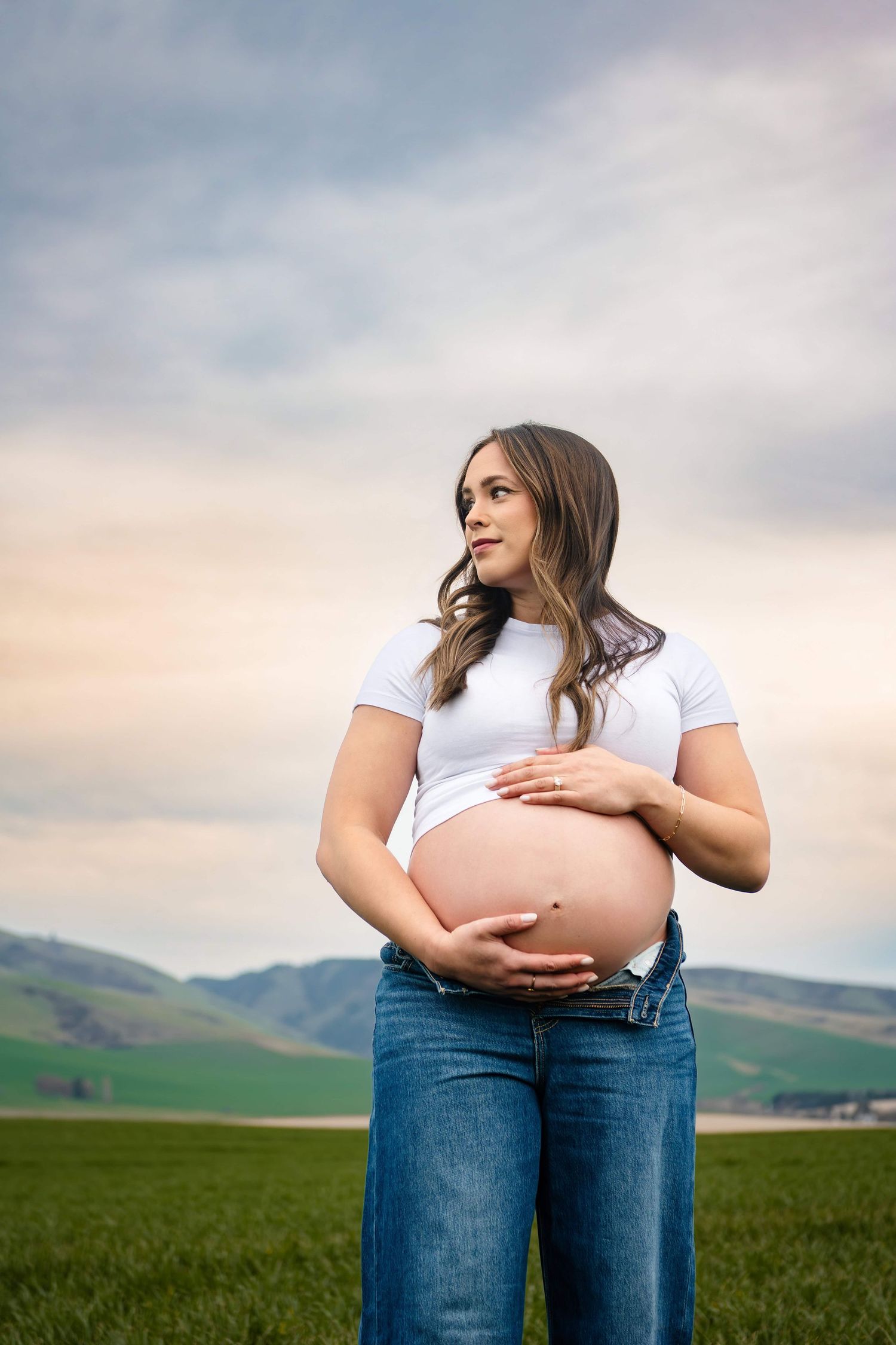 A maternity photo of a woman looking off into the distance while holding her pregnant belly during a maternity photo session in Wenatchee