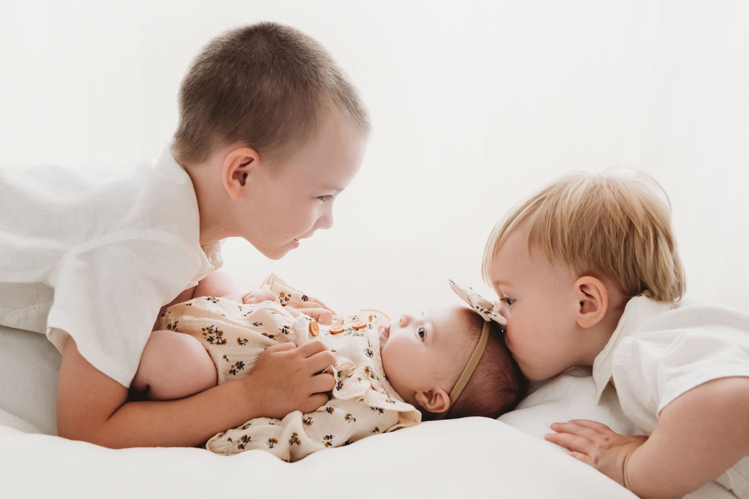 Two boys kissing their baby sister in a backlit portrait in studio.