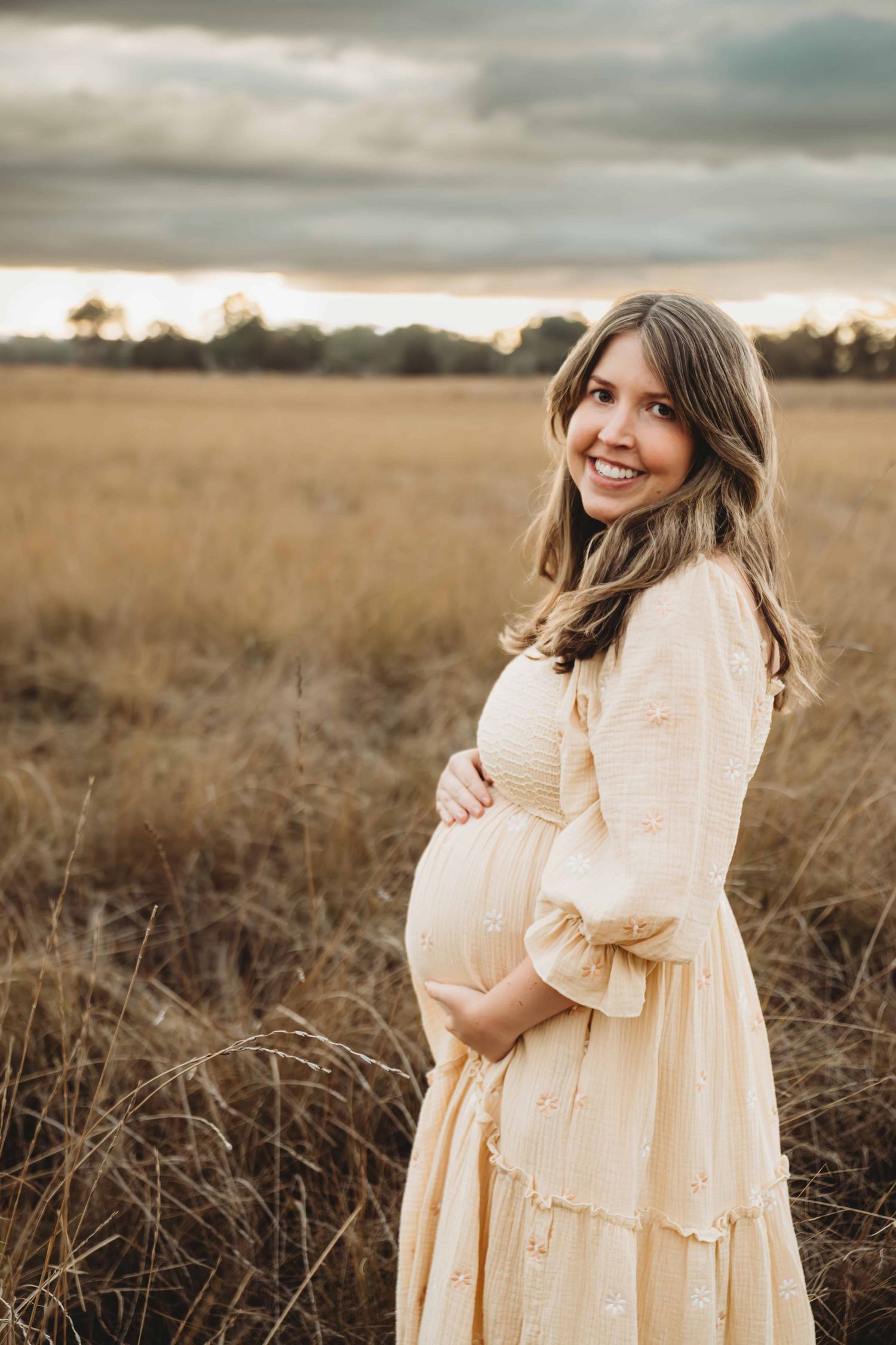 A Walla Walla maternity photographer captures a pregnant mother holding her belly and looking at the camera during sunset.
