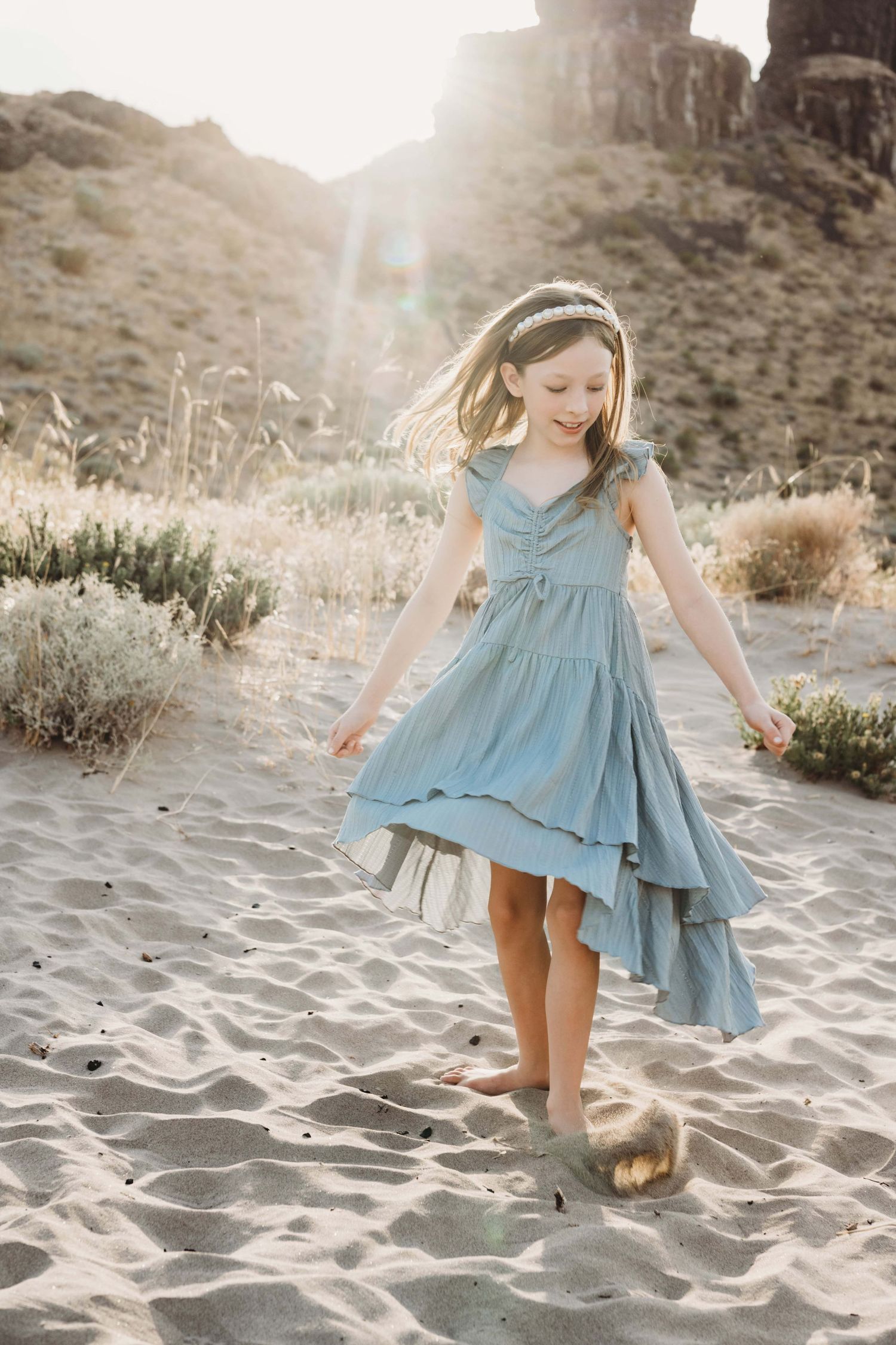 A girl twirling in a blue dress in desert scenery.