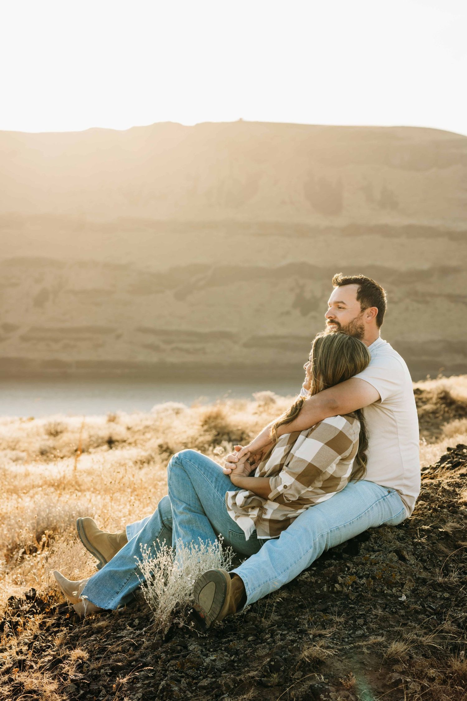 A couple sitting on a rock formation looking off into the distance during golden hour.